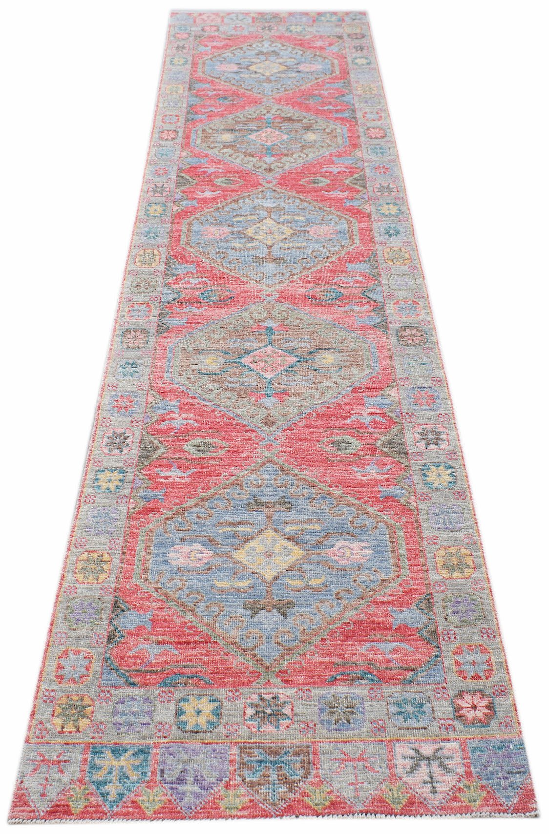 A handwoven wool runner rug featuring a repeating diamond pattern in red, blue, and beige tones.