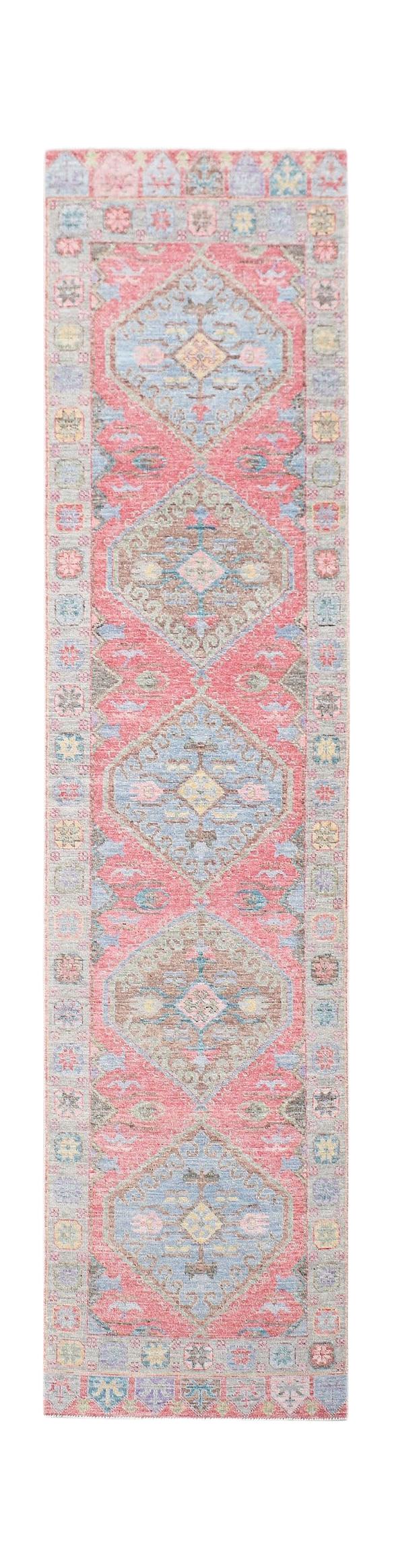 A handwoven wool runner rug featuring a repeating diamond pattern in pink, blue, and tan tones.