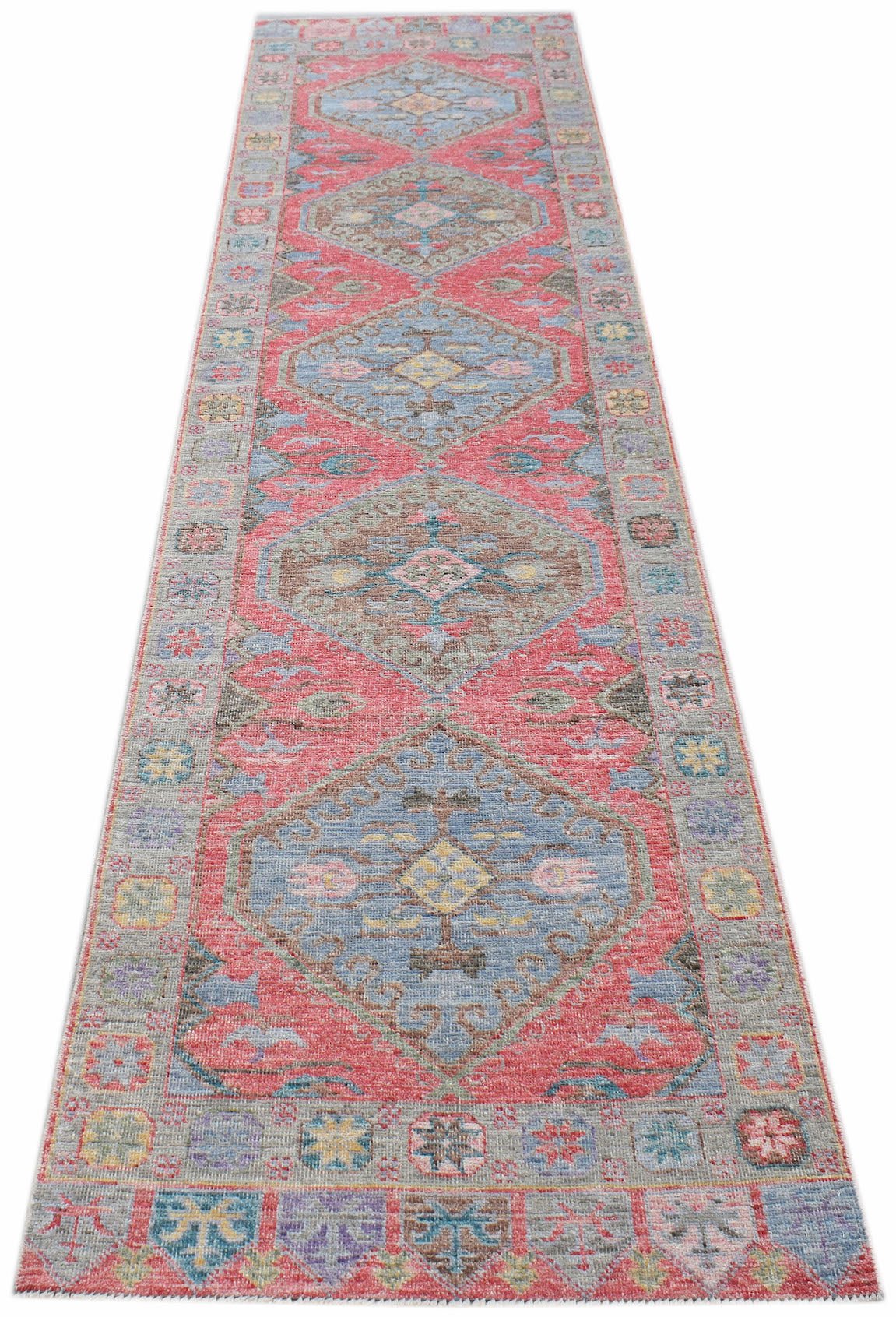 A handwoven wool runner rug featuring a repeating diamond pattern in shades of blue, pink, and grey.
