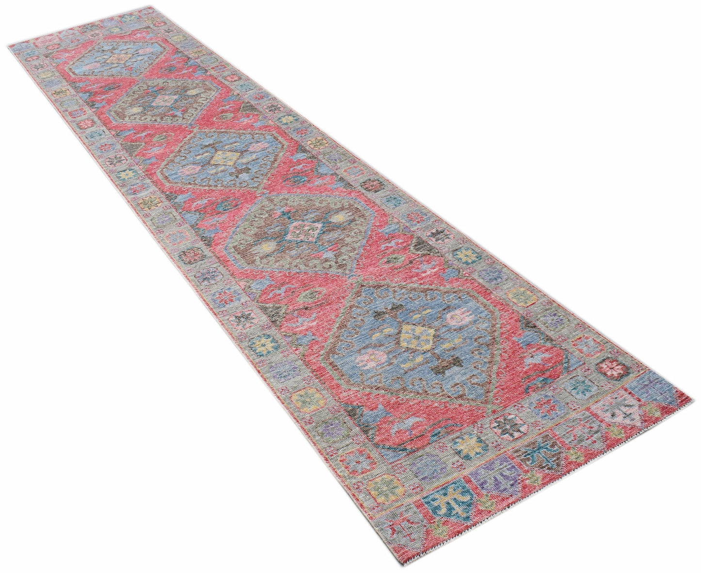 A handwoven wool runner rug featuring a traditional Oushak pattern in red, blue, and grey tones.