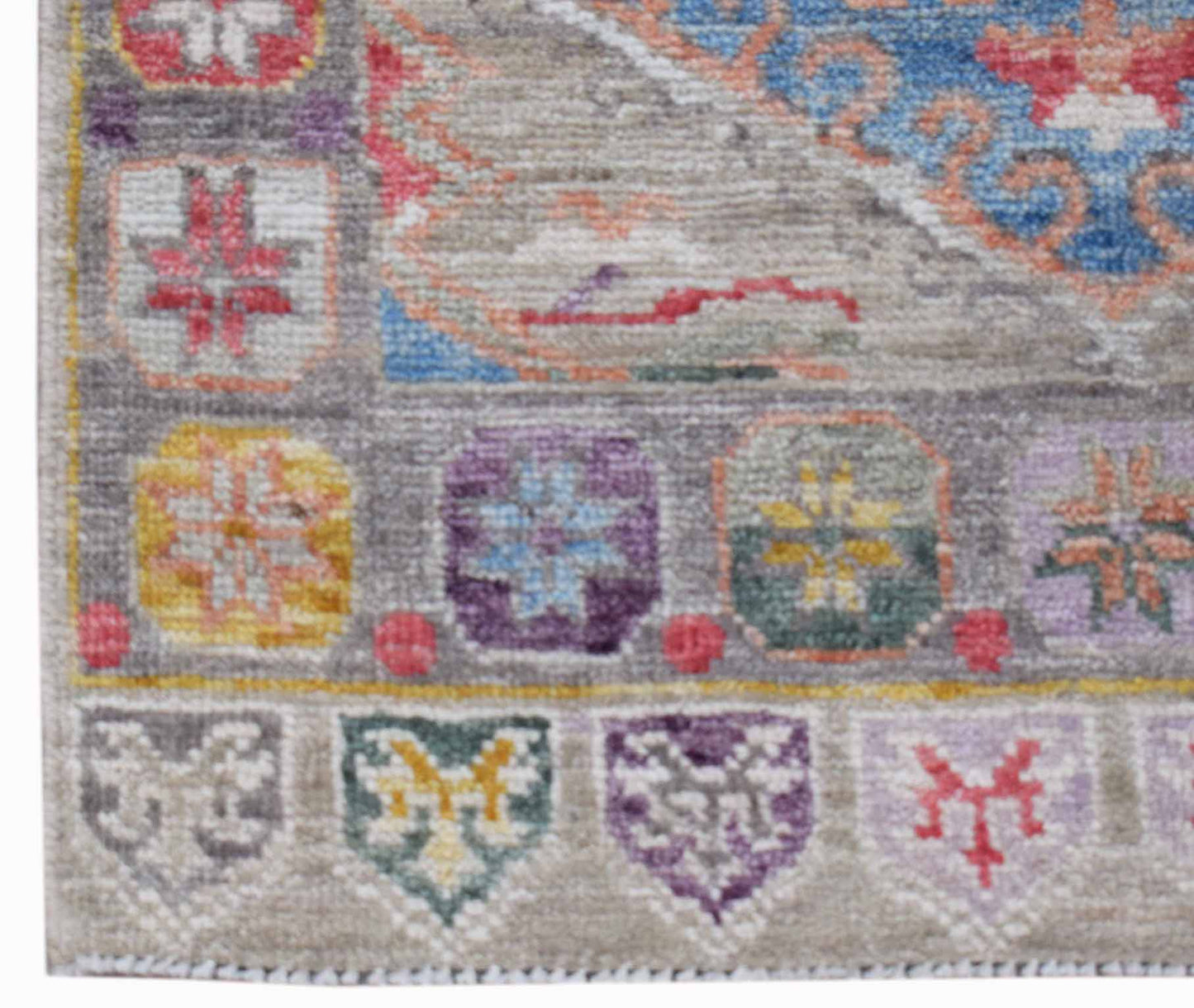 A handwoven transitional Oushak rug featuring a grey border with colorful geometric motifs.