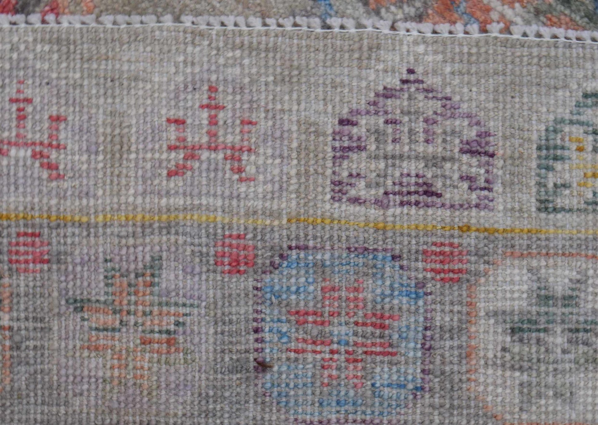 A close-up view of a handwoven wool rug featuring geometric patterns in muted, earthy tones.