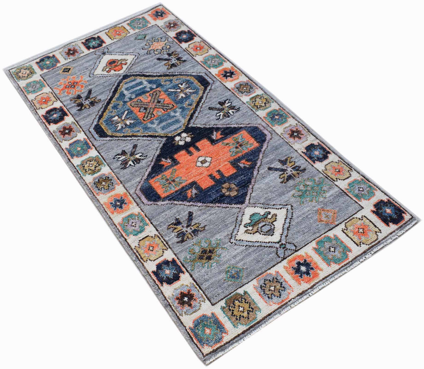 A rectangular handwoven wool rug featuring a grey field with geometric patterns in orange and blue.