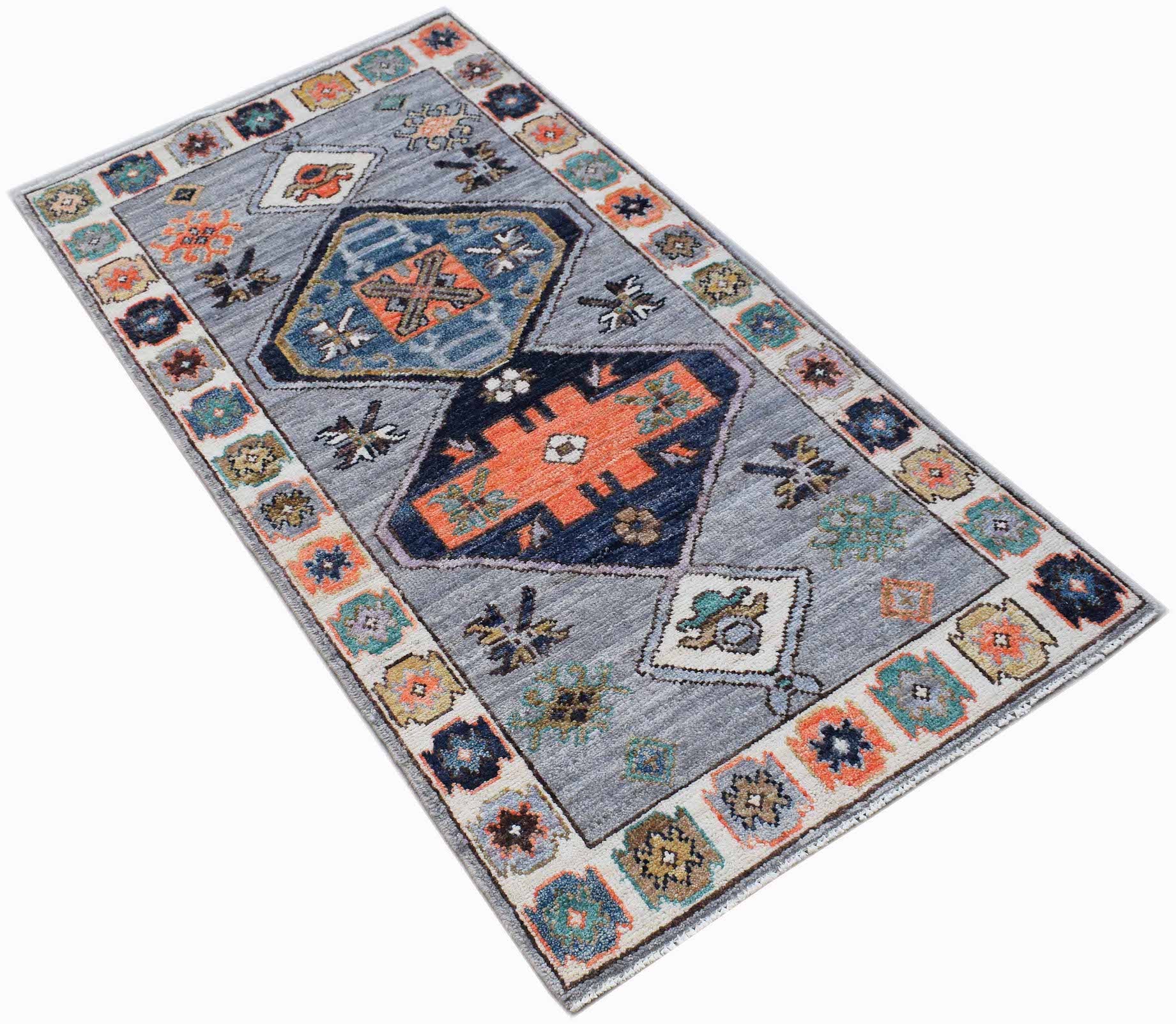 A rectangular handwoven wool rug featuring a grey field with geometric patterns in orange and blue.