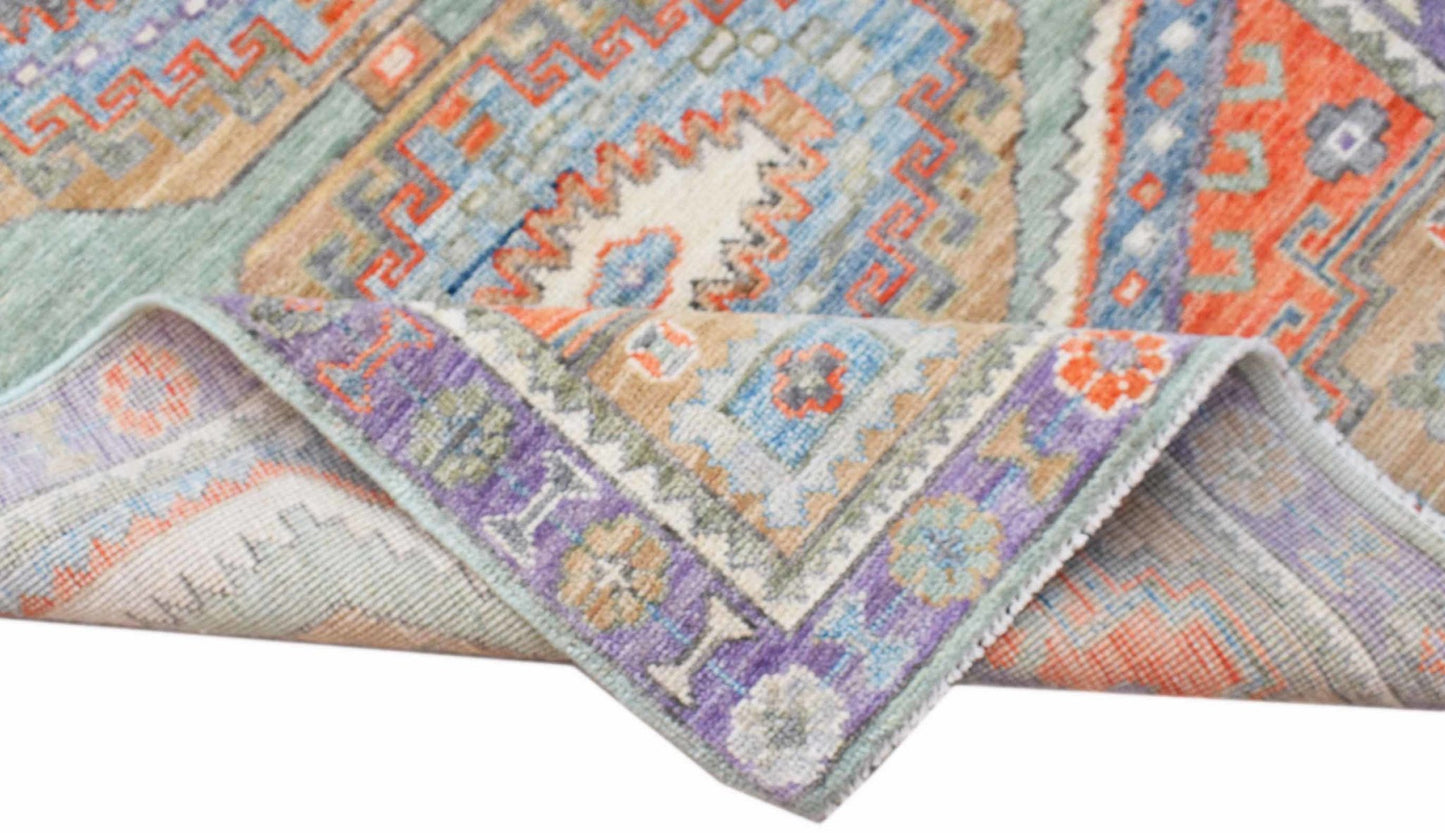 A handwoven transitional Oushak rug featuring a colorful geometric pattern and a folded corner.