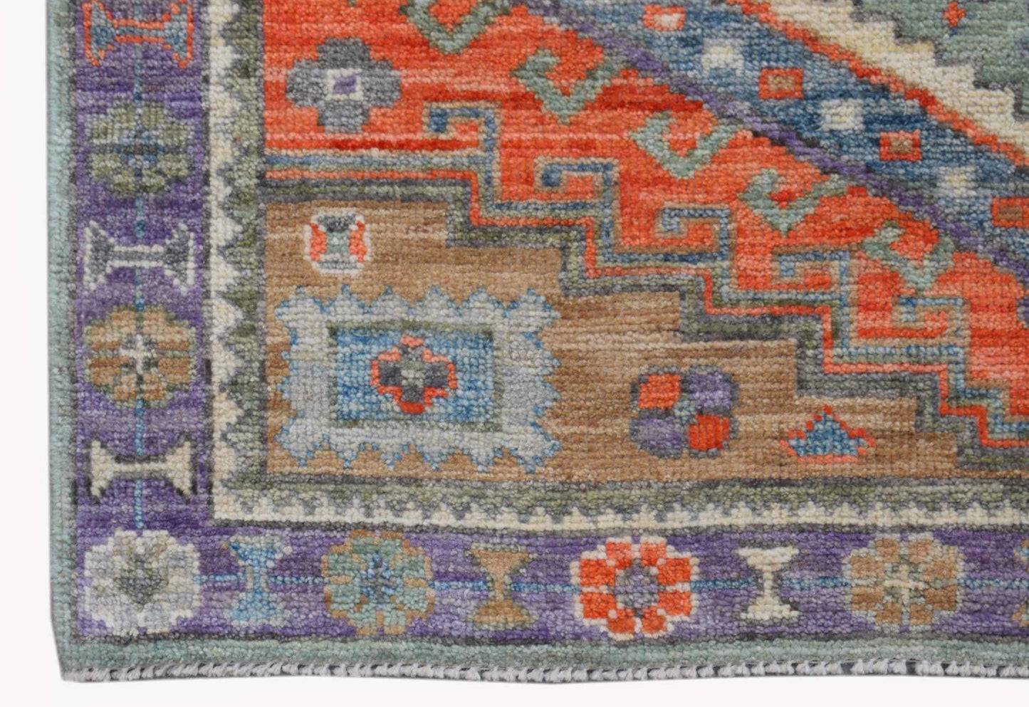 A handwoven wool Oushak rug featuring a geometric pattern in orange, blue, and purple tones.