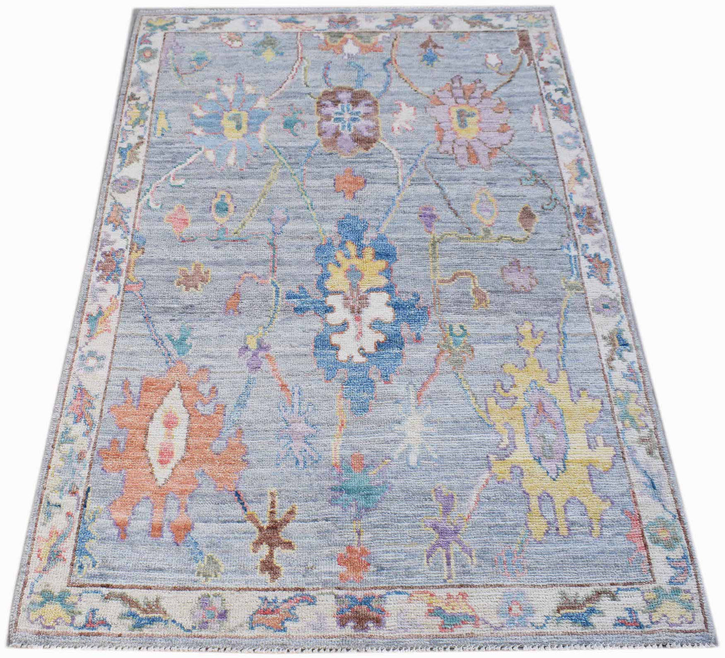 A handwoven transitional Oushak rug featuring a floral pattern in soft colors on a blue background.