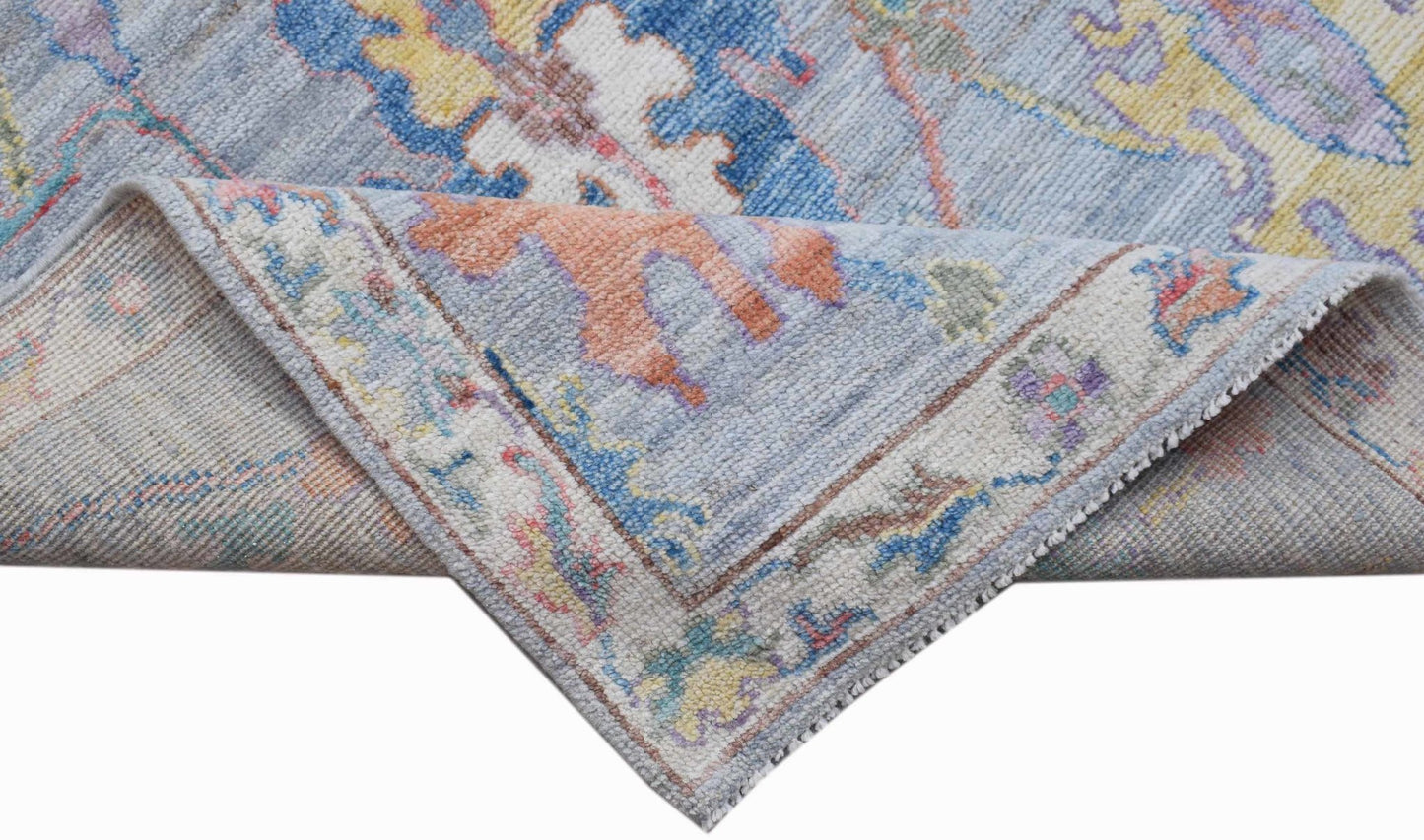 A handwoven transitional Oushak rug featuring a floral pattern in soft blue and pastel tones.