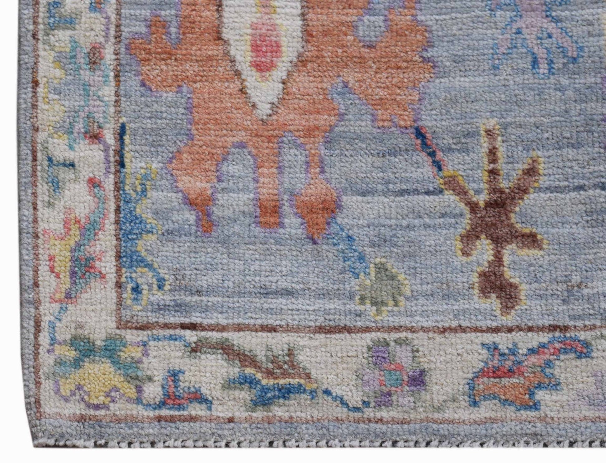 A handwoven transitional Oushak rug featuring a floral pattern in blue, orange, and cream tones.