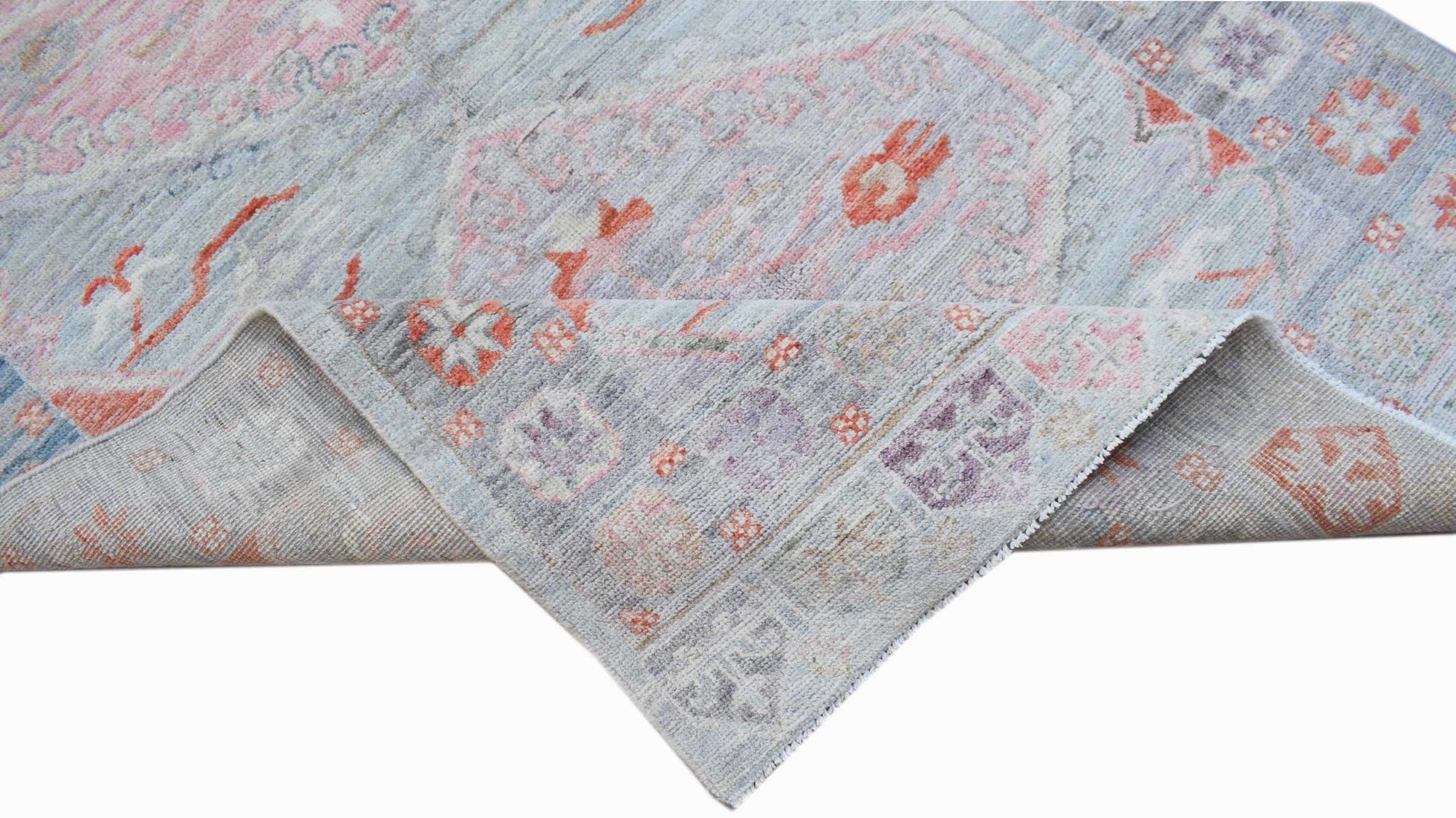 A handwoven transitional Oushak rug featuring a floral pattern in soft blue, pink, and orange tones.