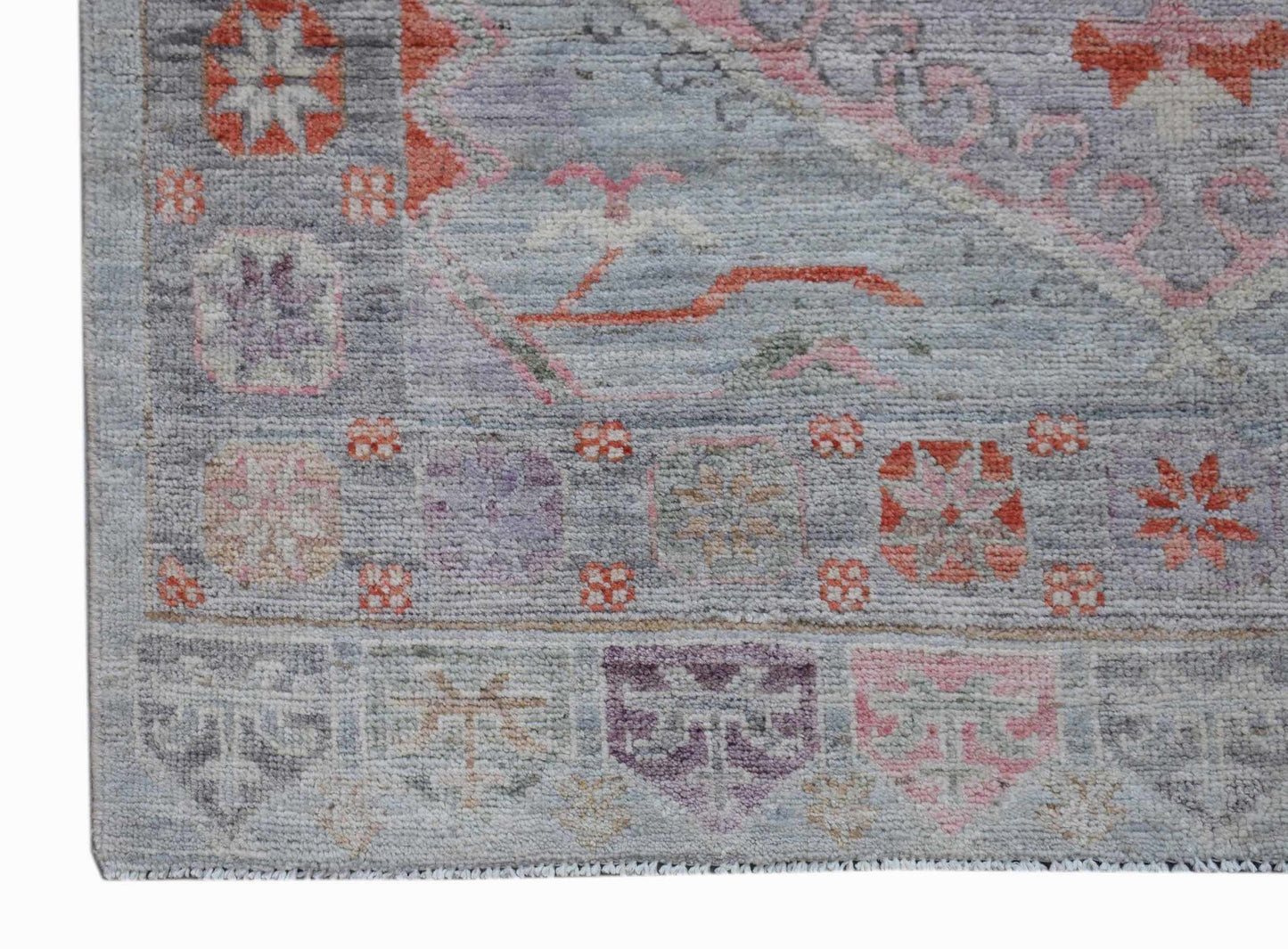 A handwoven transitional Oushak rug featuring a floral pattern in soft blue, pink, and orange tones.