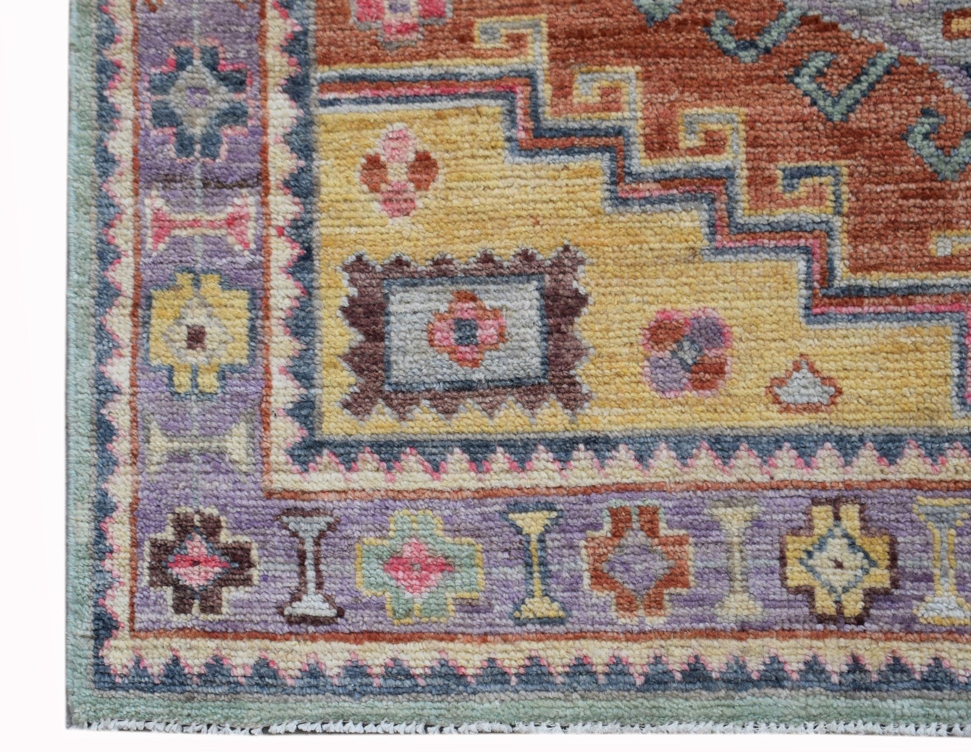 A handwoven transitional Oushak rug featuring a geometric pattern in shades of purple, yellow, and red.