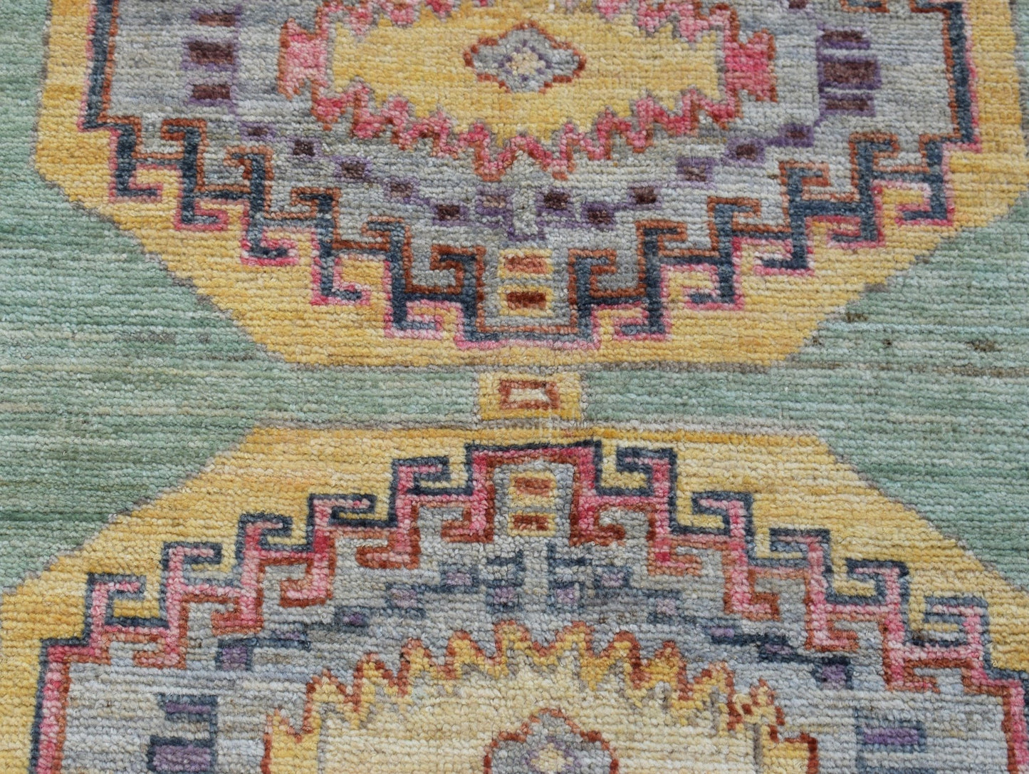 A handwoven wool Oushak rug featuring geometric medallions in yellow, pink, and blue tones.