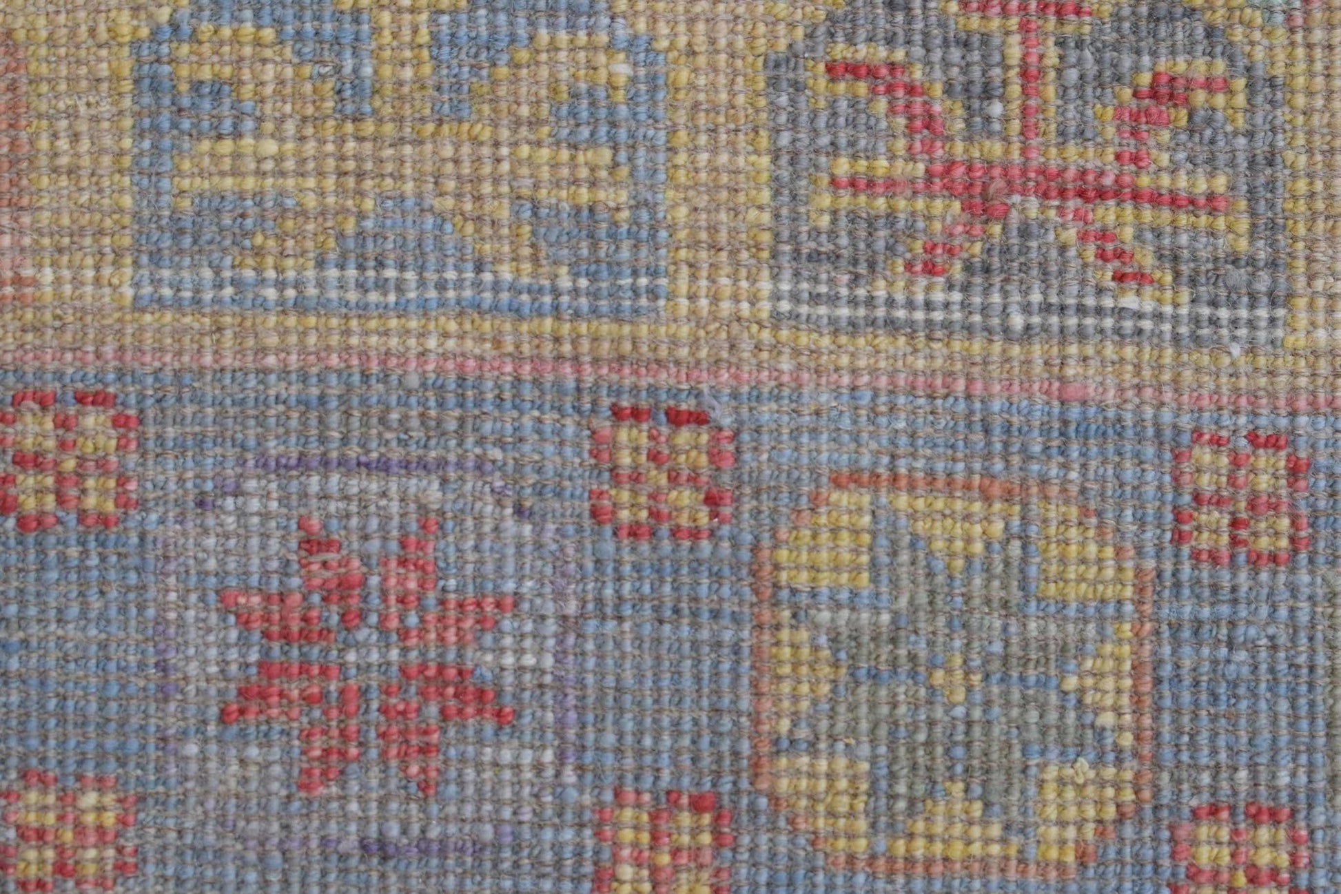 A close-up of a handwoven wool rug featuring a geometric pattern in blue, yellow, and red tones.