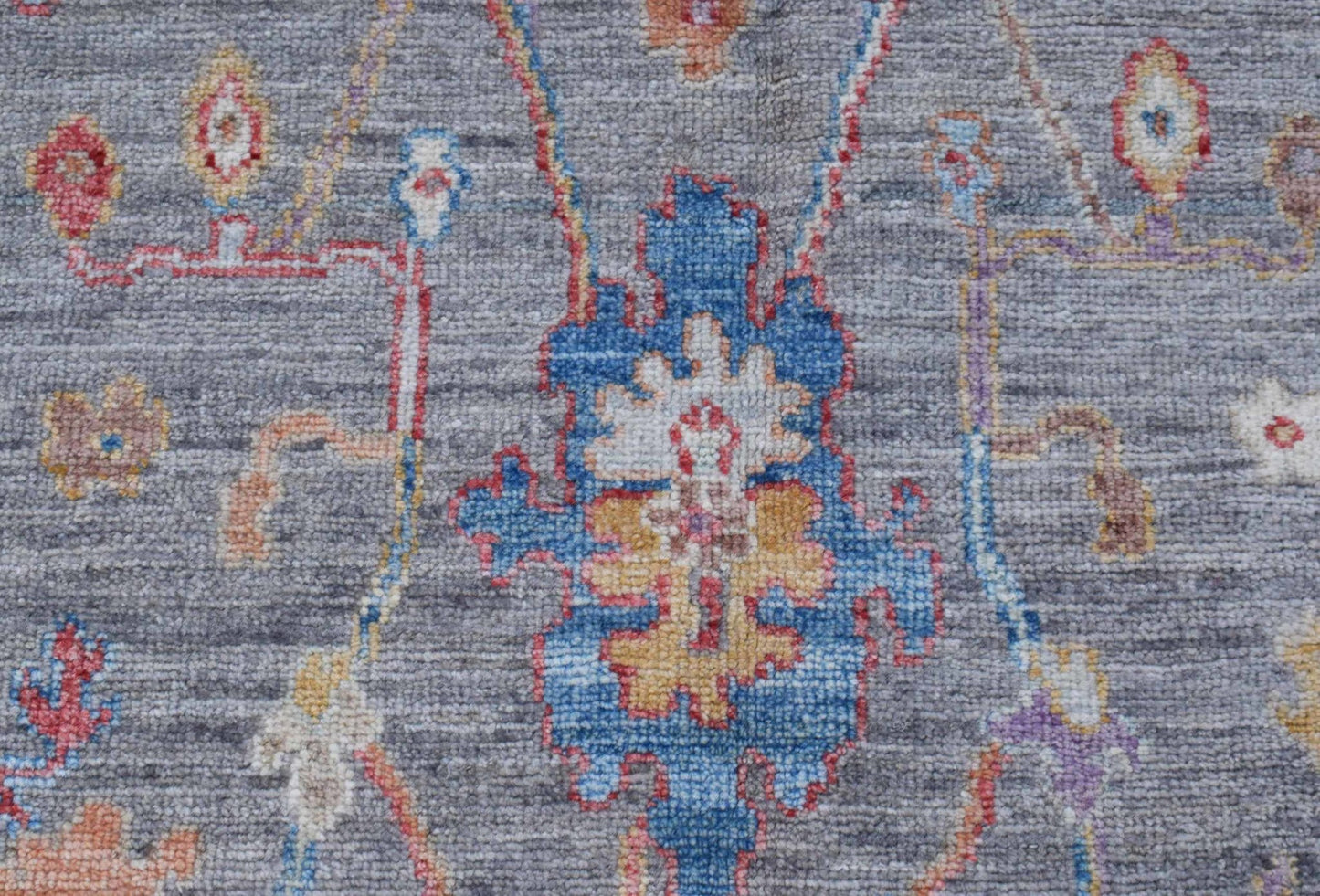 A handwoven transitional Oushak rug featuring a floral pattern in blue, yellow, and red on grey.