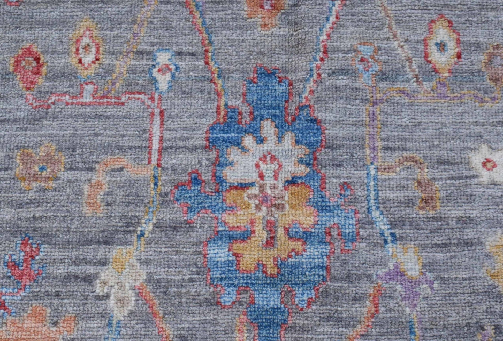 A handwoven transitional Oushak rug featuring a floral pattern in blue, yellow, and red on grey.