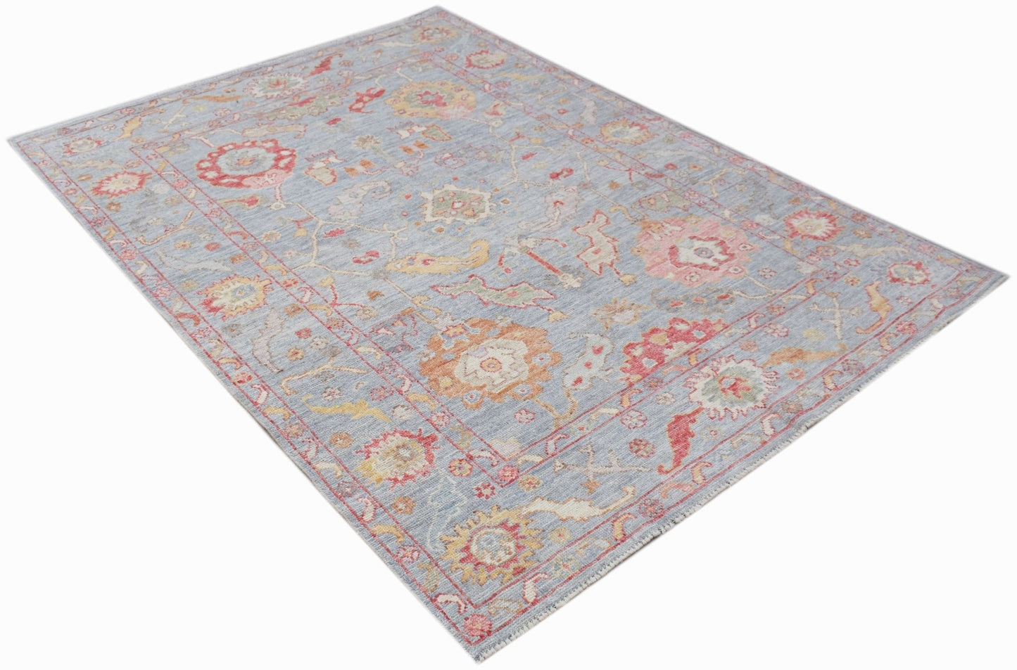 A handwoven transitional Oushak rug featuring a floral pattern in soft blue, red, and gold tones.