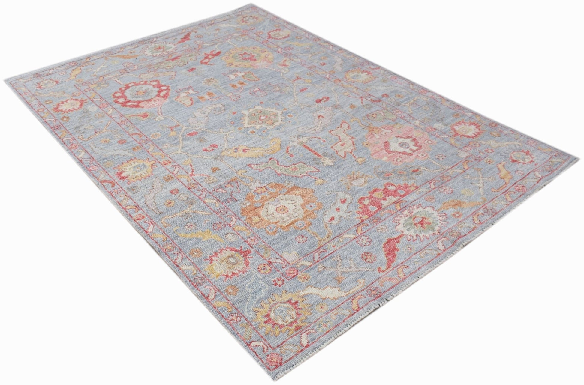 A handwoven transitional Oushak rug featuring a floral pattern in soft blue, red, and gold tones.