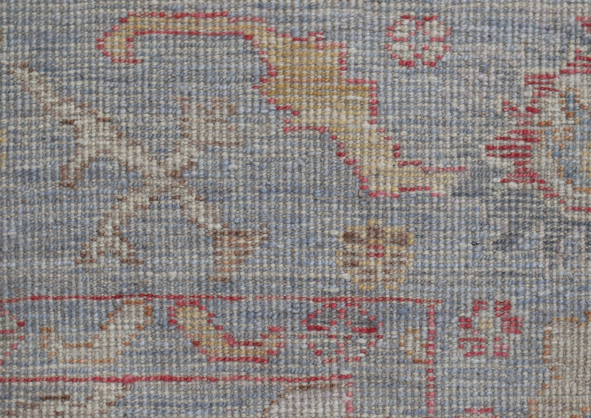 A close-up of a handwoven Oushak rug featuring a floral pattern in muted blue, red, and gold tones.