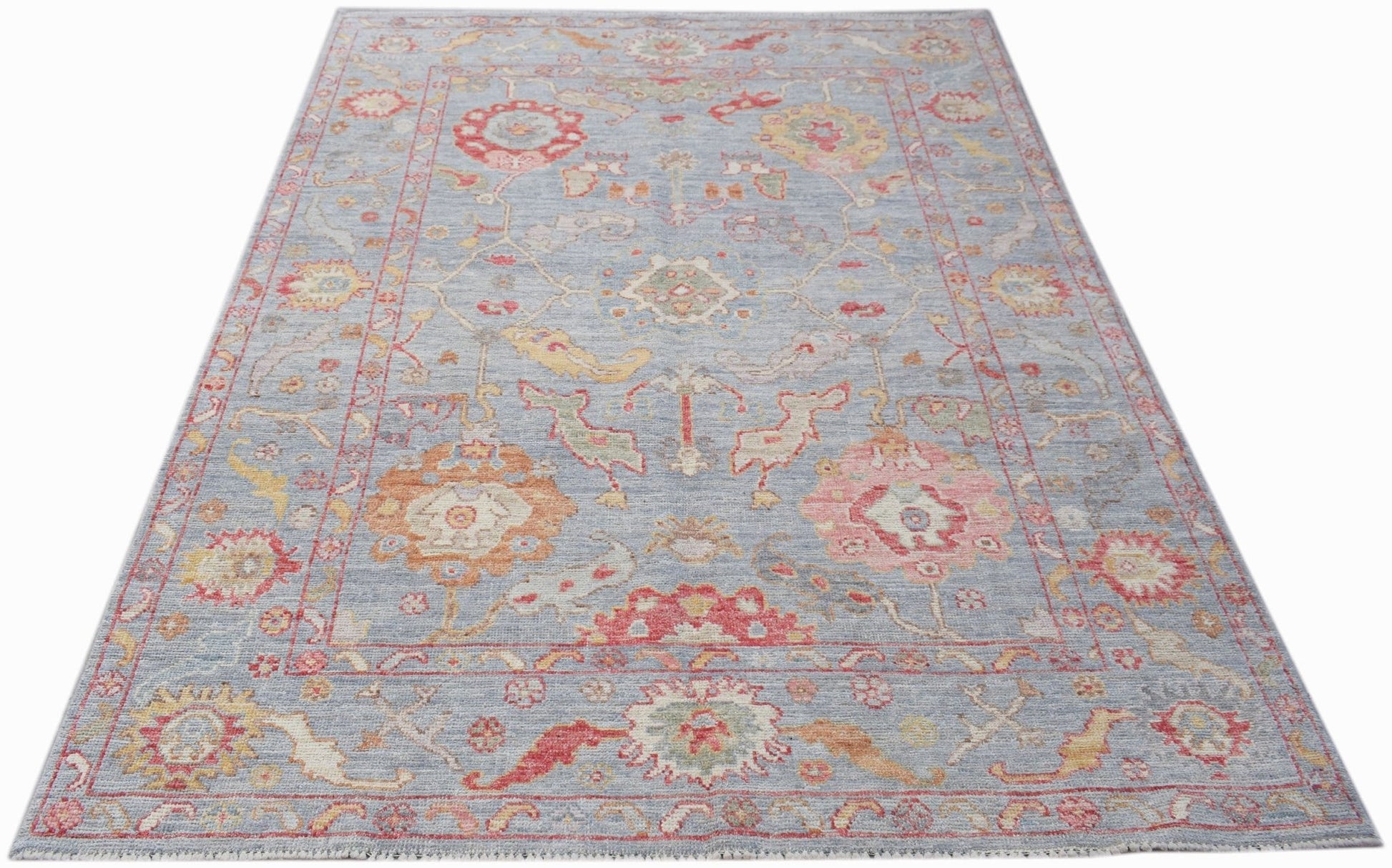 A handwoven transitional Oushak rug featuring a floral pattern in soft colors on a blue background.