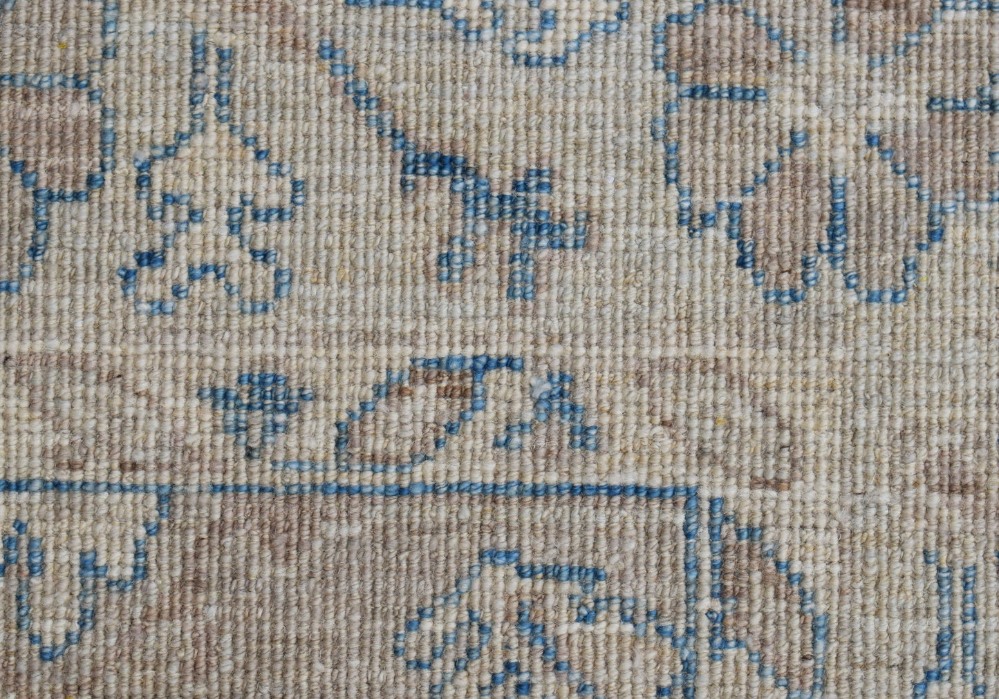 A close-up of a handwoven transitional Oushak rug featuring a blue floral pattern on a beige wool.