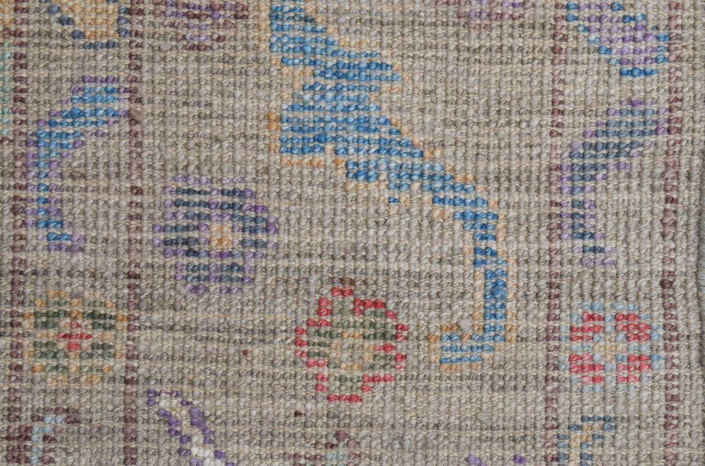 A handwoven wool Oushak rug featuring a floral pattern in blue, red, and purple on a beige field.