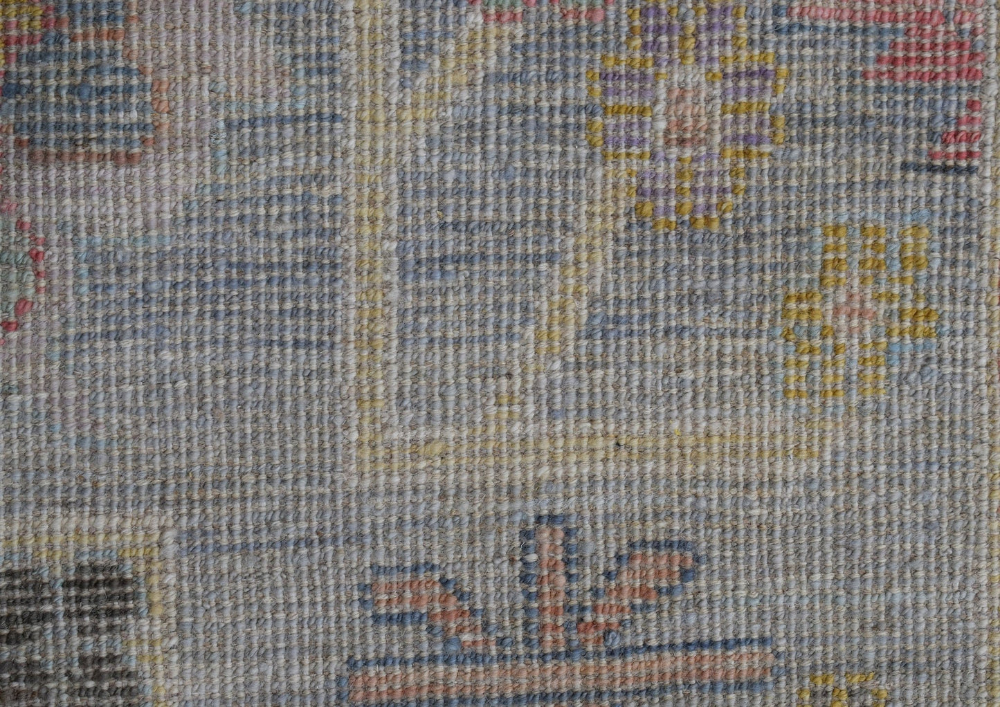 A close-up of a handwoven wool rug featuring a transitional floral pattern in muted tones.