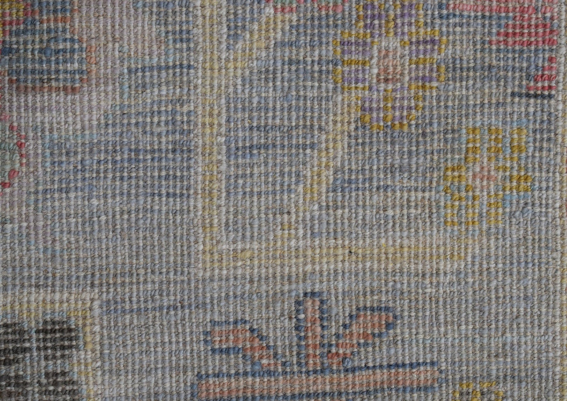 A close-up of a handwoven wool rug featuring a transitional floral pattern in muted tones.