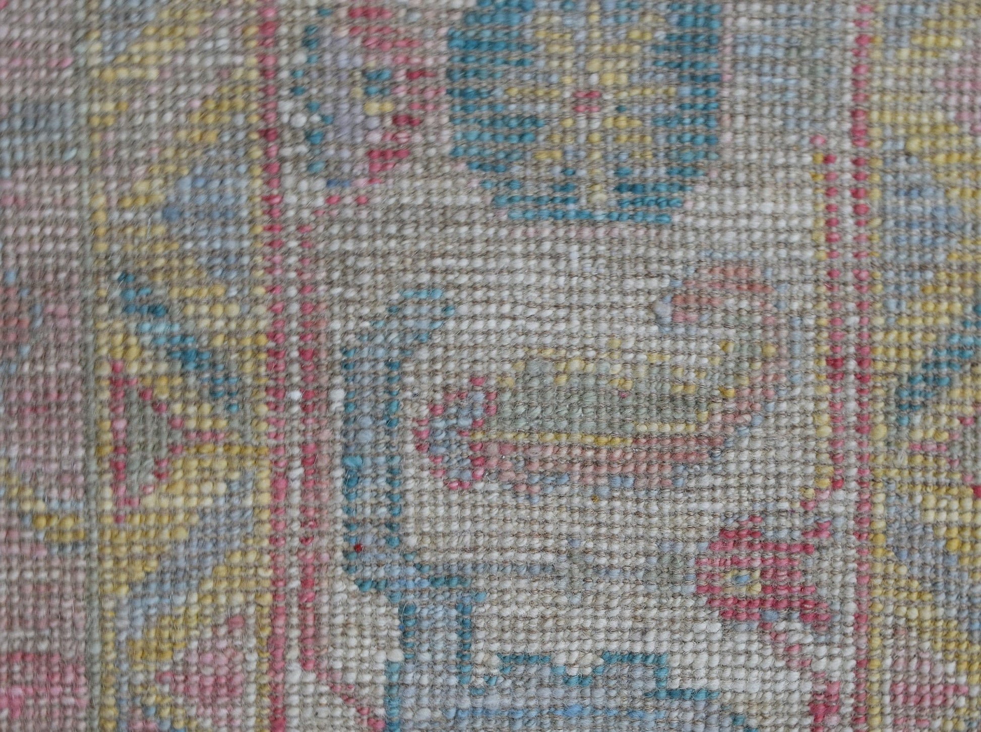 A close-up view of a handwoven wool rug featuring a transitional floral pattern in soft colors.