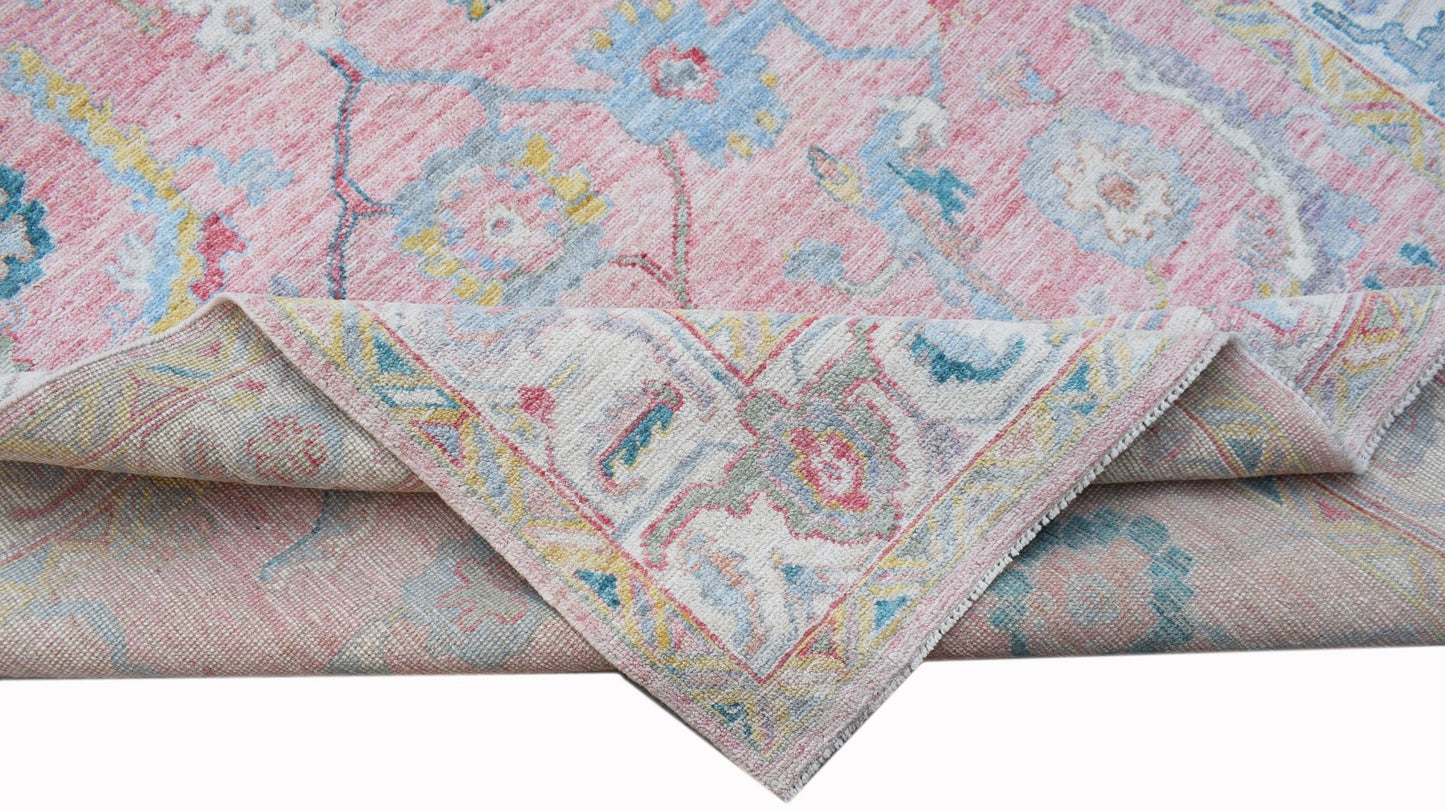 A handwoven transitional Oushak rug featuring a floral pattern in pink, blue, and yellow tones.