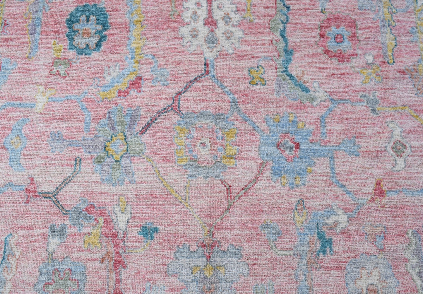 A handwoven transitional Oushak rug featuring a floral pattern in soft pink, blue, and yellow tones.