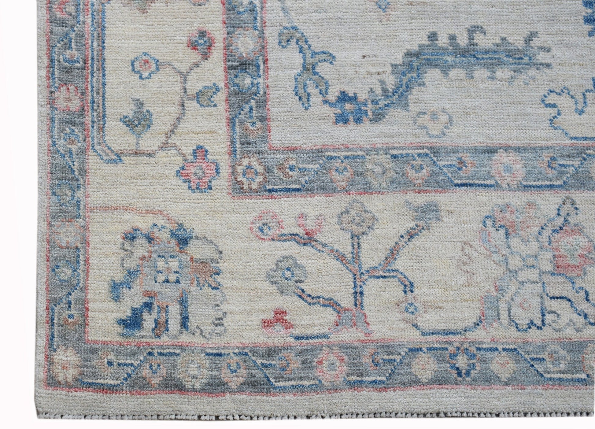 A handwoven transitional Oushak rug featuring a floral pattern in blue and pink on a cream field.