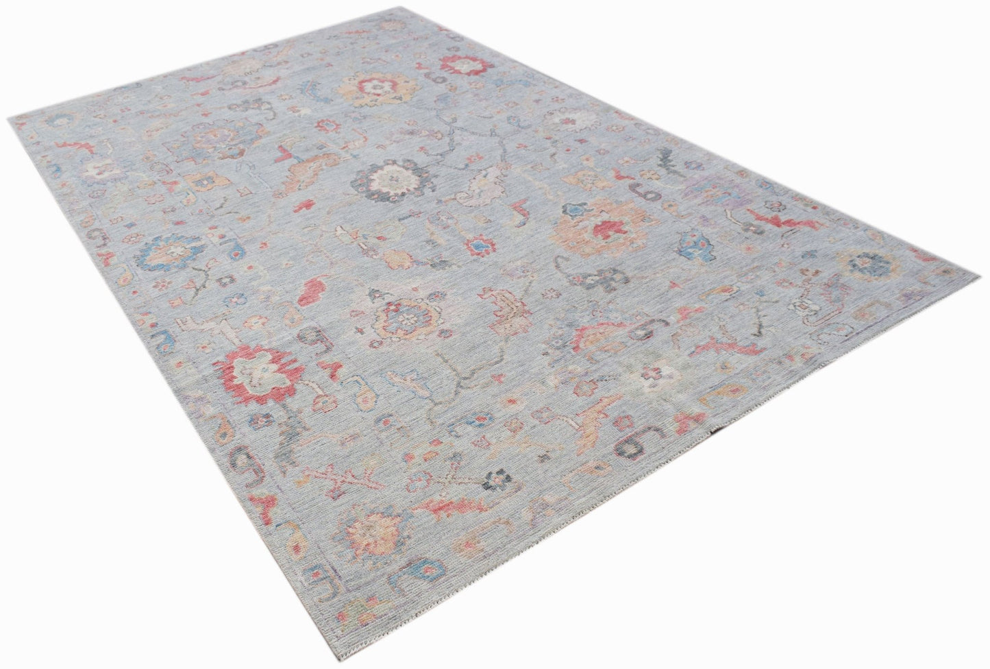A handwoven transitional Oushak rug featuring a floral pattern in soft blue and muted tones.