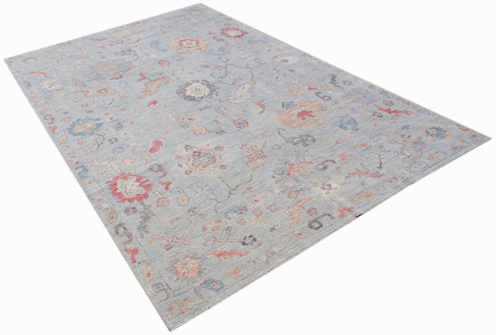 A handwoven transitional Oushak rug featuring a floral pattern in soft blue and muted tones.