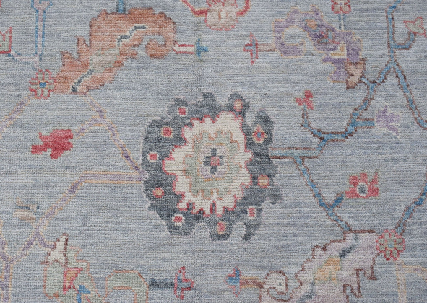 A handwoven transitional Oushak rug featuring a floral pattern in muted tones on a blue background.