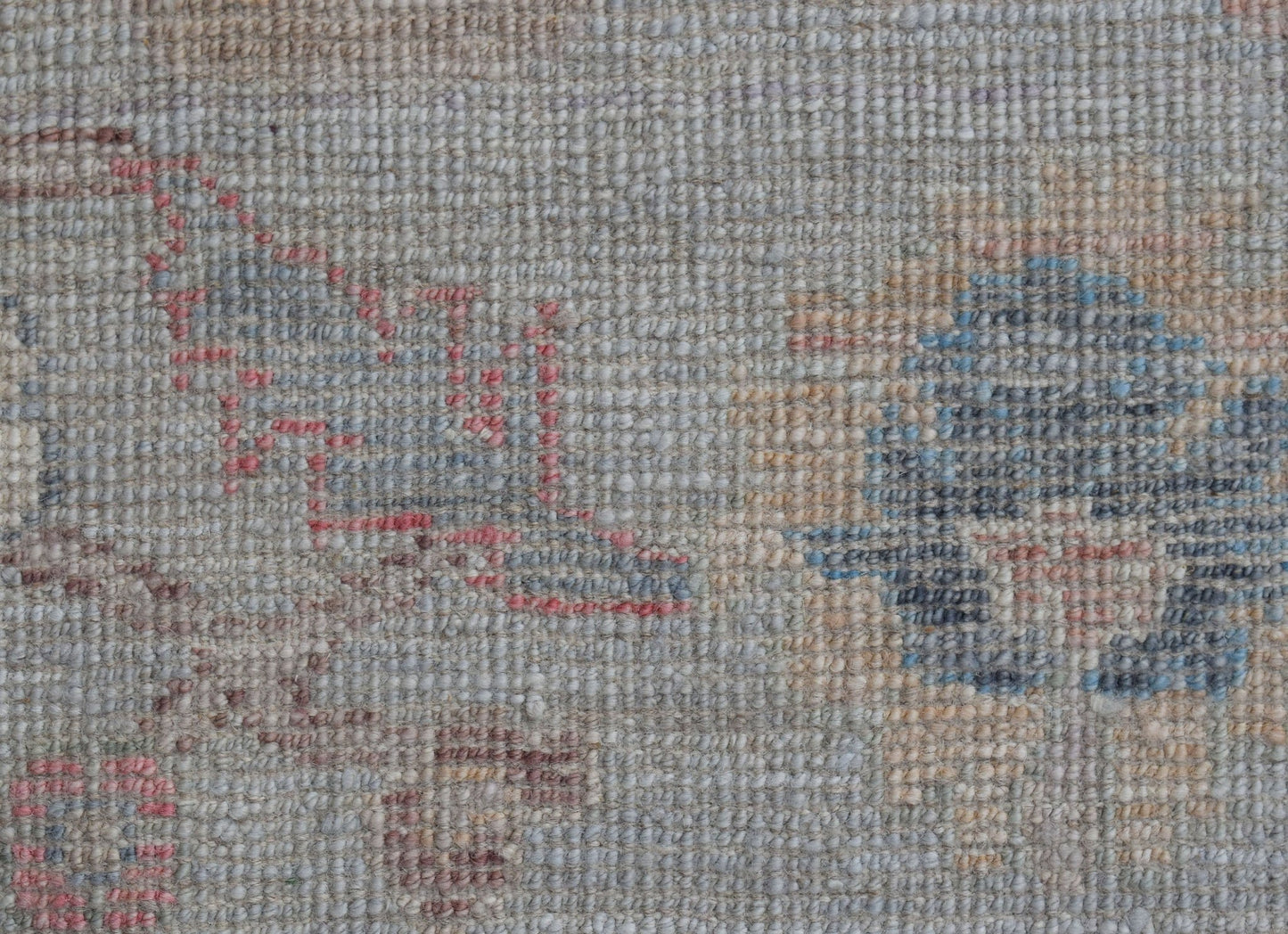 A close-up of a handwoven wool rug featuring a faded floral pattern in soft blue and pink tones.