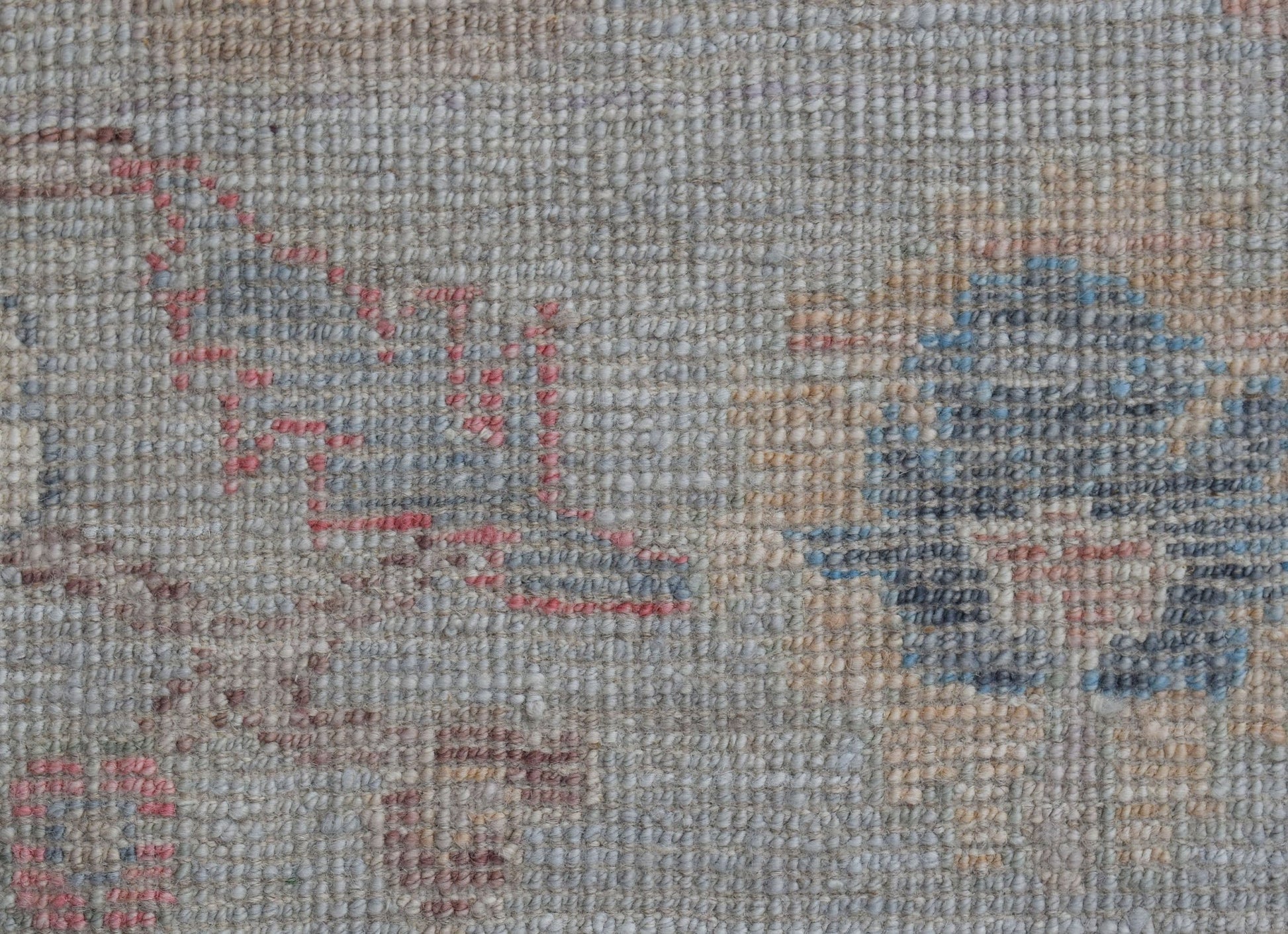 A close-up of a handwoven wool rug featuring a faded floral pattern in soft blue and pink tones.