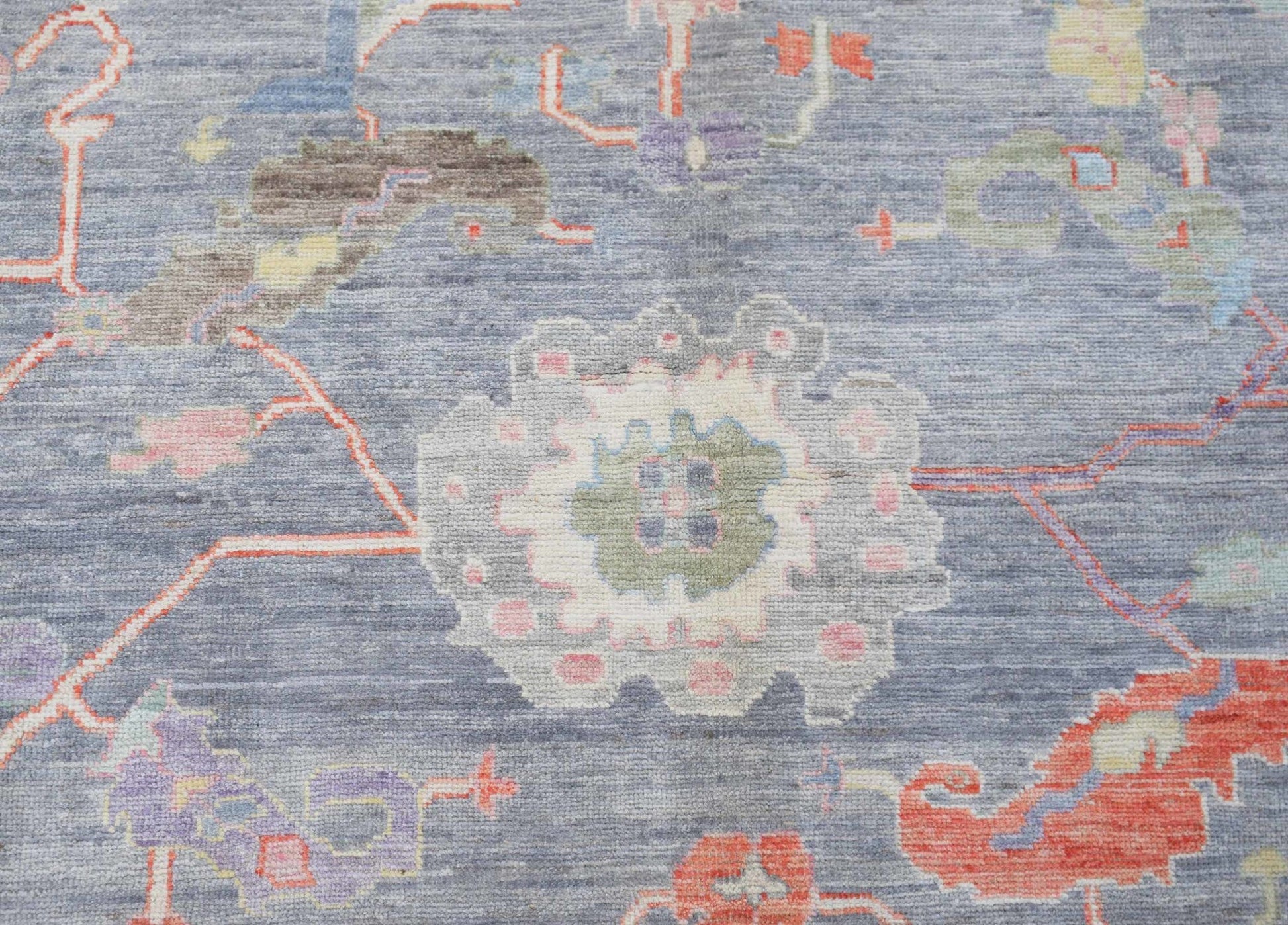 A handwoven transitional Oushak rug featuring a floral pattern in soft tones on a blue background.