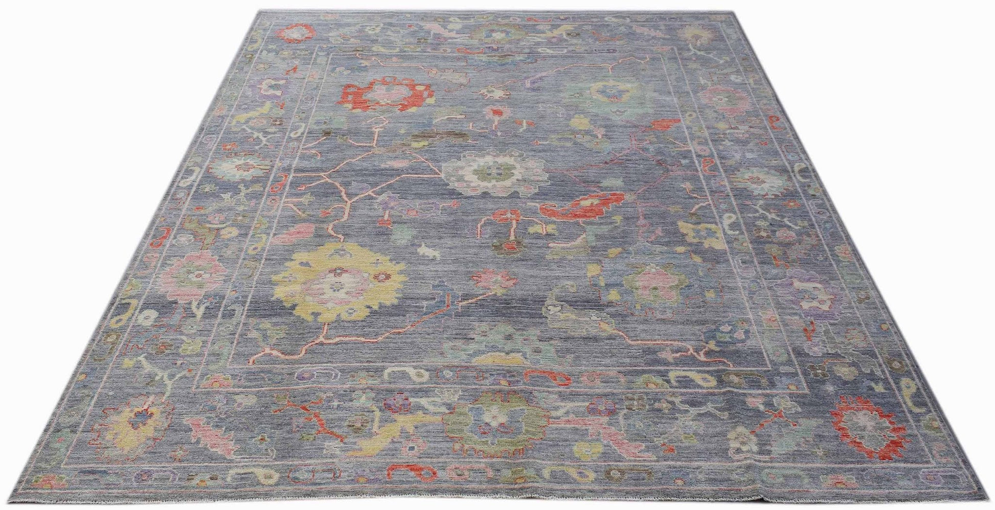 A handwoven transitional Oushak rug featuring a floral pattern in muted tones on a blue background.