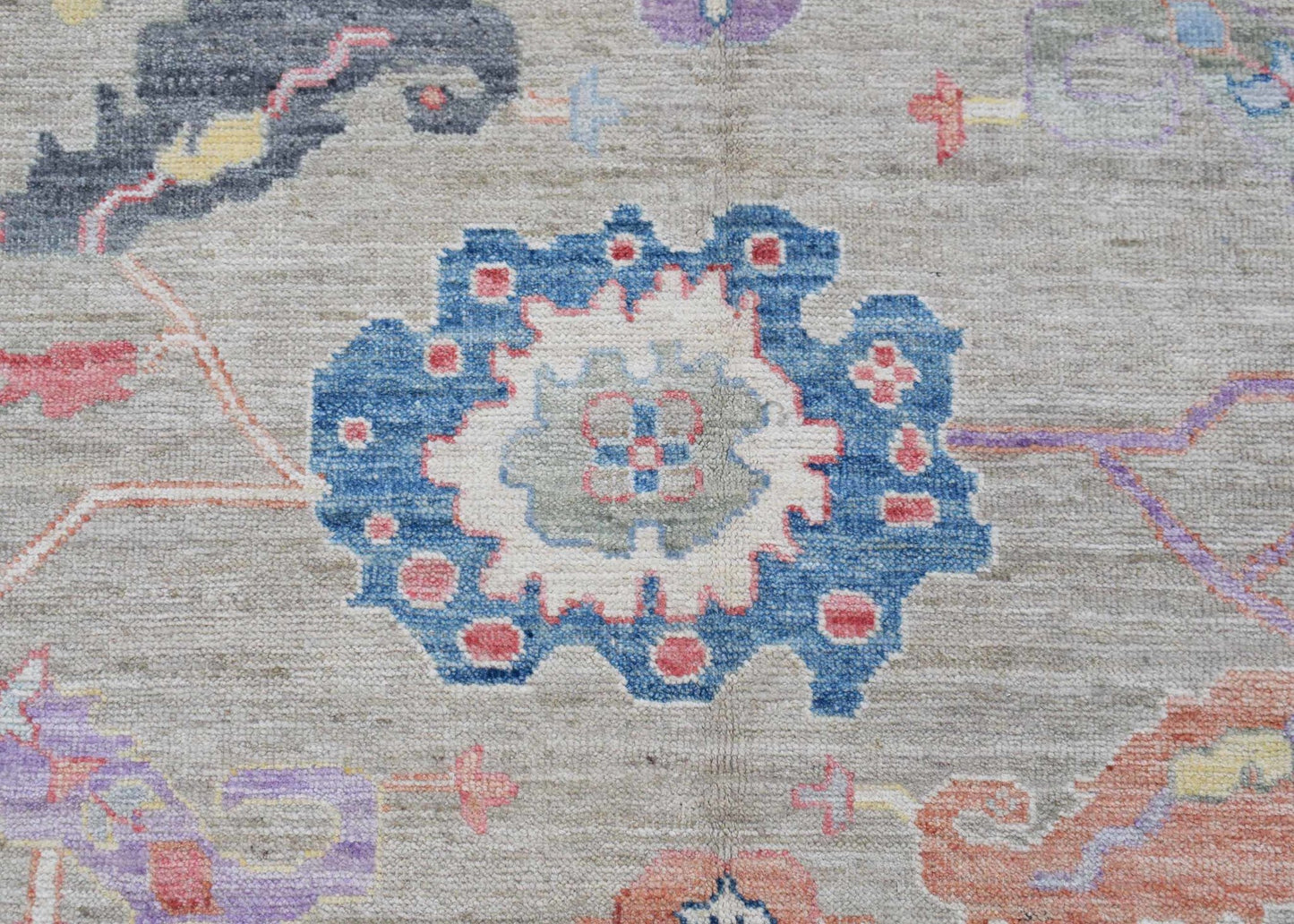 A handwoven transitional Oushak rug featuring a floral pattern in blue, pink, and grey tones.