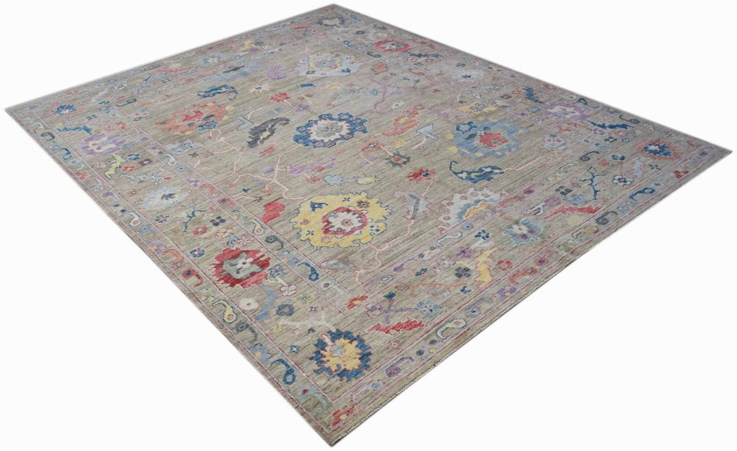 A handwoven transitional Oushak rug featuring a floral pattern in vibrant colors on a gray field.