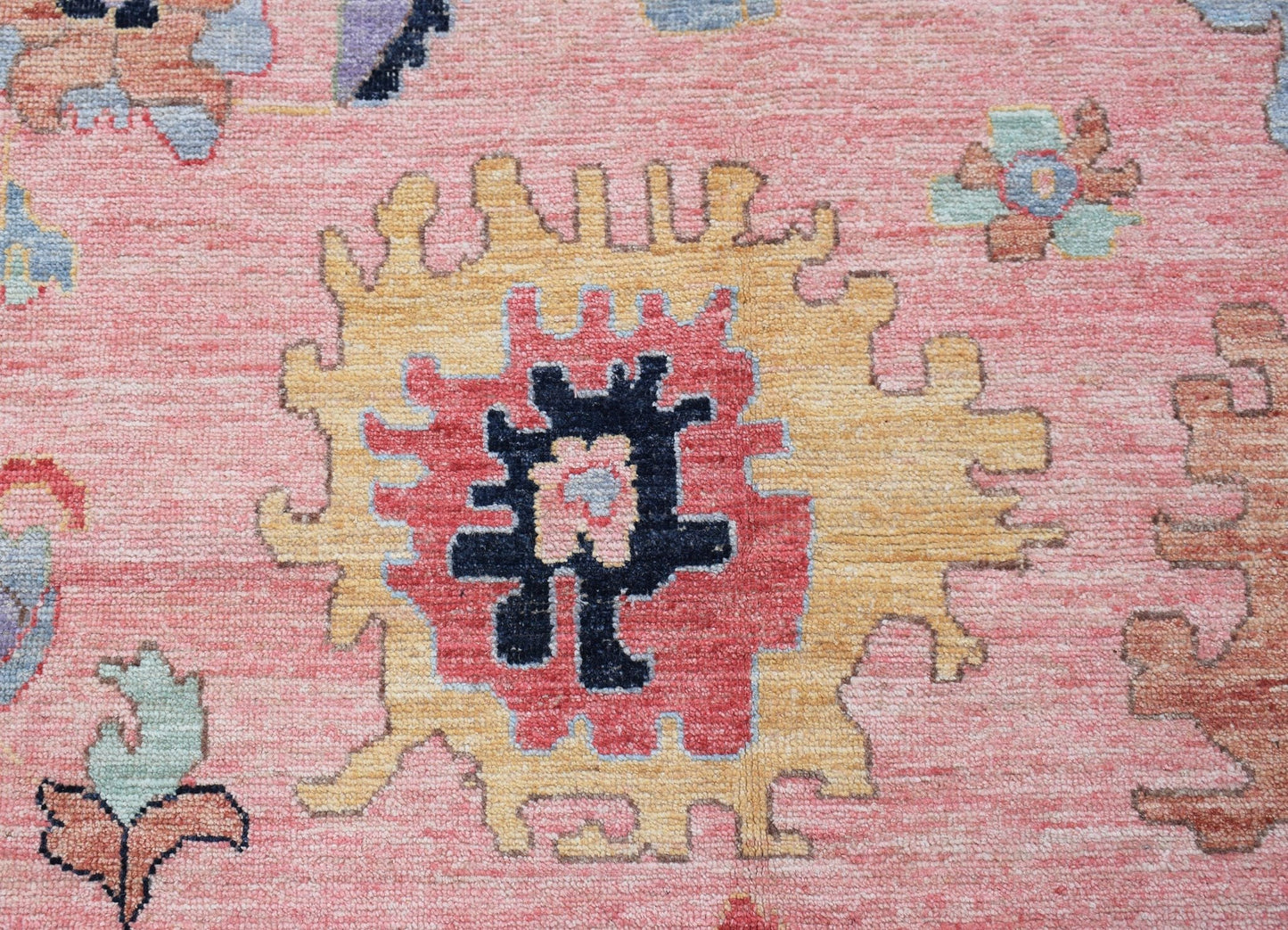 A handwoven transitional Oushak rug featuring a central floral medallion in pink, yellow, and blue.