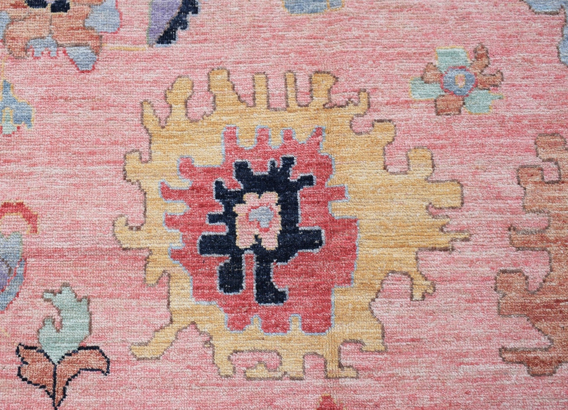 A handwoven transitional Oushak rug featuring a central floral medallion in pink, yellow, and blue.