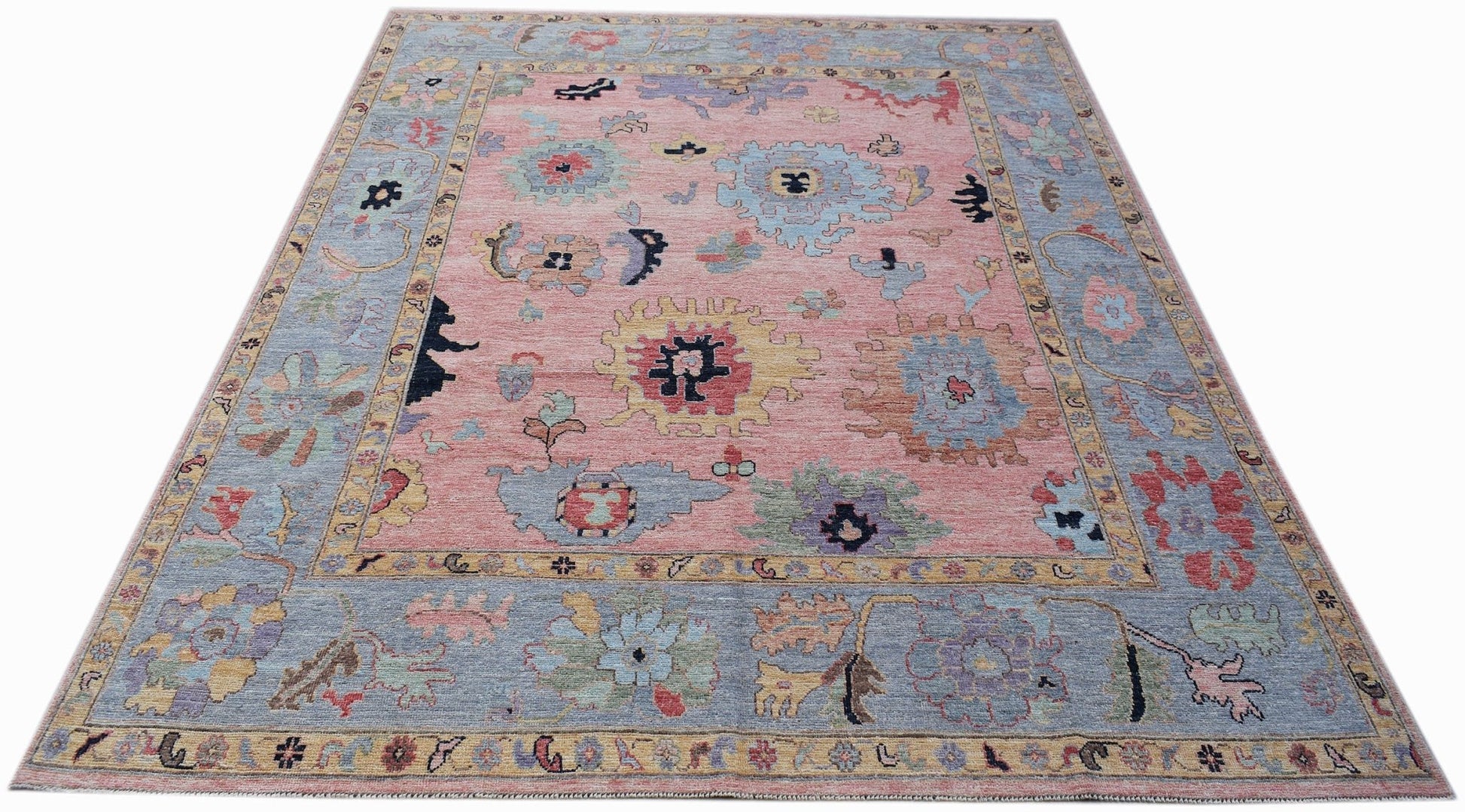 A transitional Oushak rug featuring a floral pattern in muted tones on a pink field.