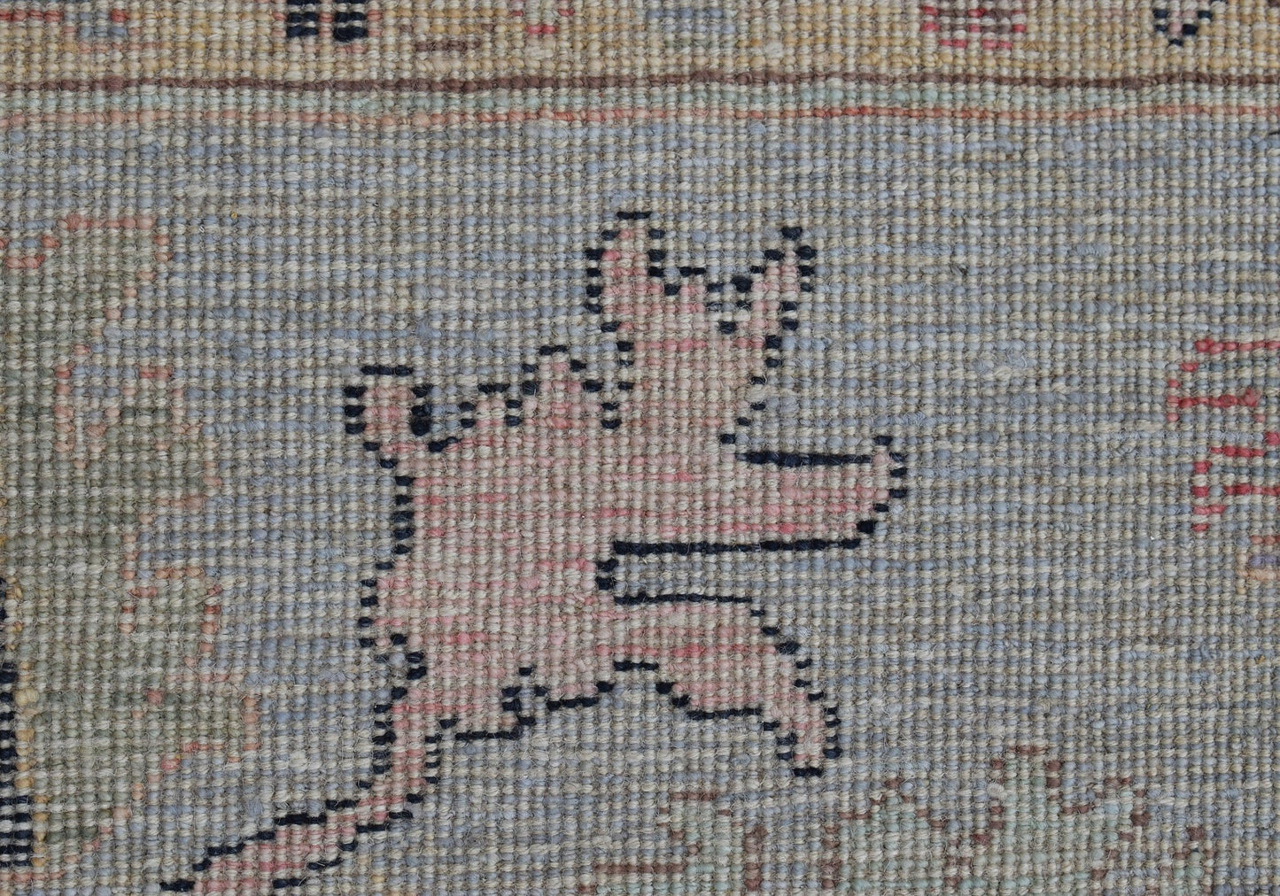 A close-up of a handwoven wool rug featuring a stylized pink animal motif on a blue background.