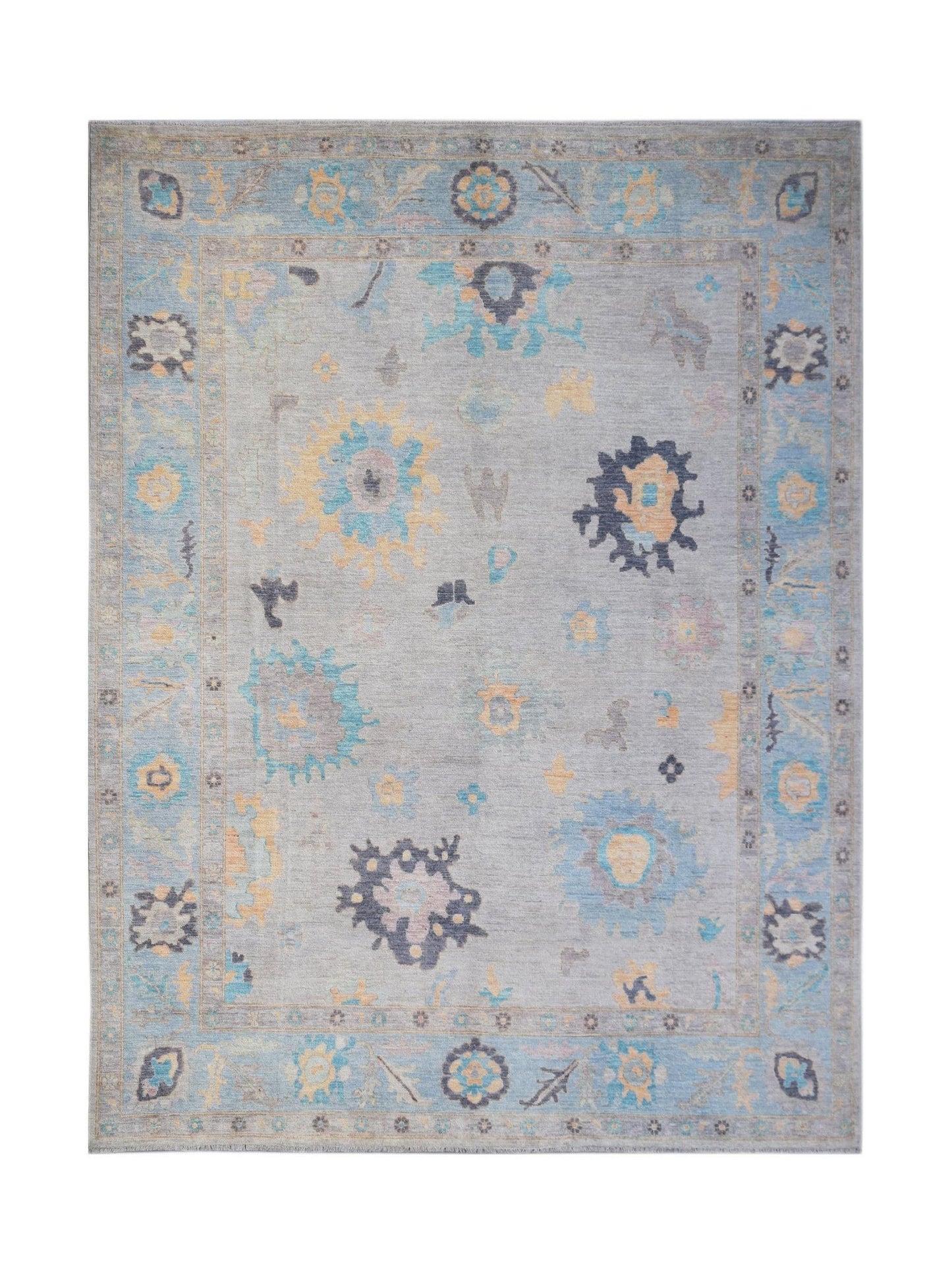 A transitional Oushak rug featuring a light grey field with scattered floral motifs in blue and gold.
