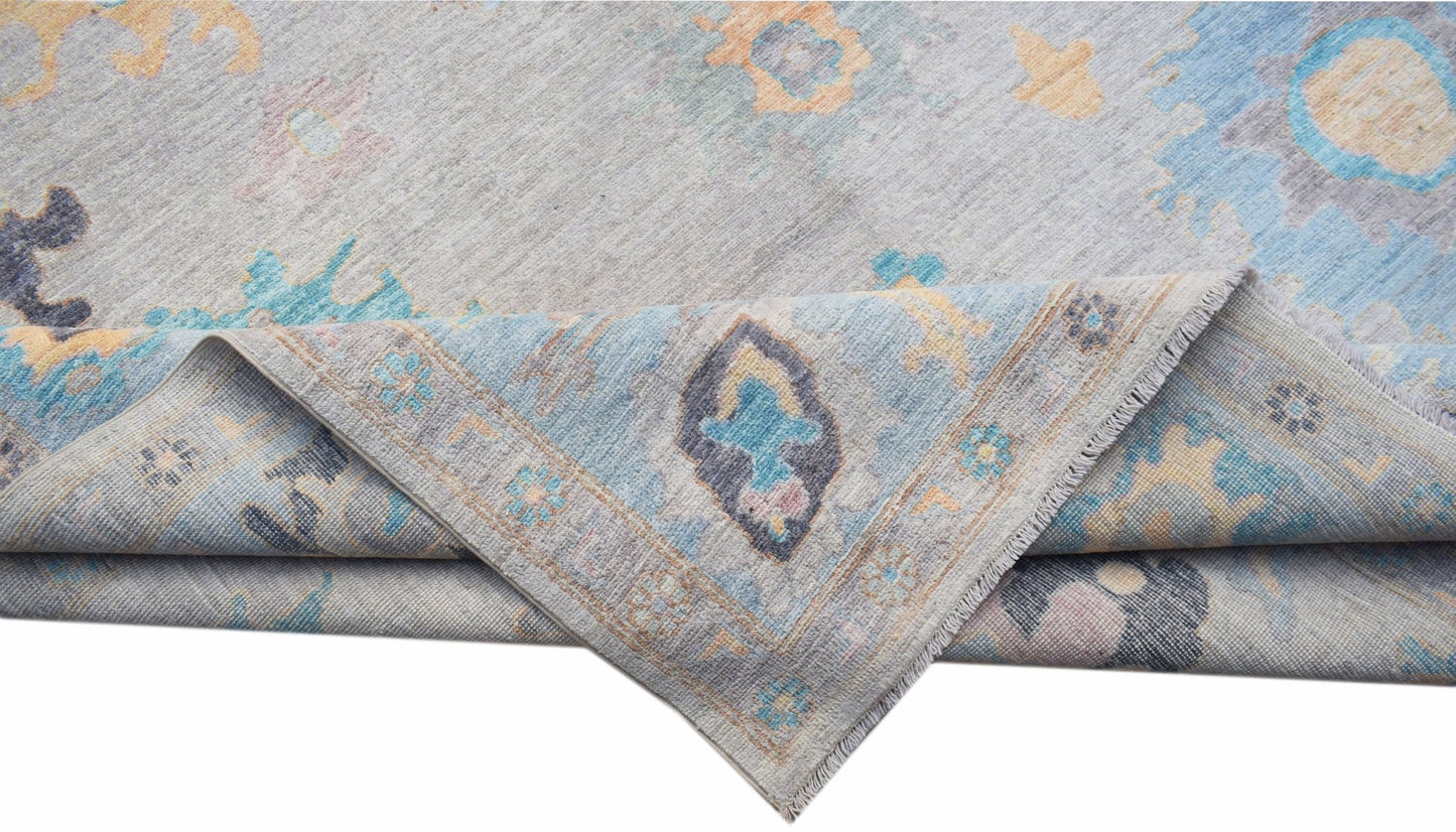 A handwoven transitional Oushak rug featuring a floral pattern in blue, grey, and soft yellow tones.
