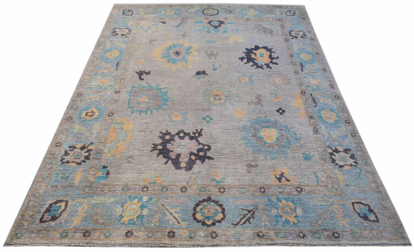 A handwoven transitional Oushak rug featuring a floral pattern in blue, yellow, and grey tones.