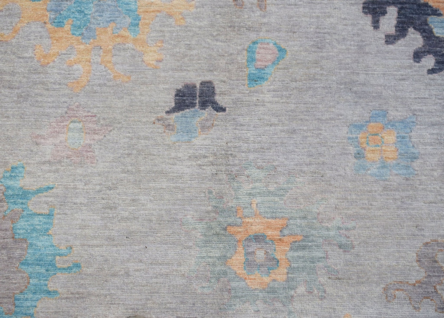 A handwoven transitional Oushak rug featuring a floral pattern in blue and orange on a grey field.