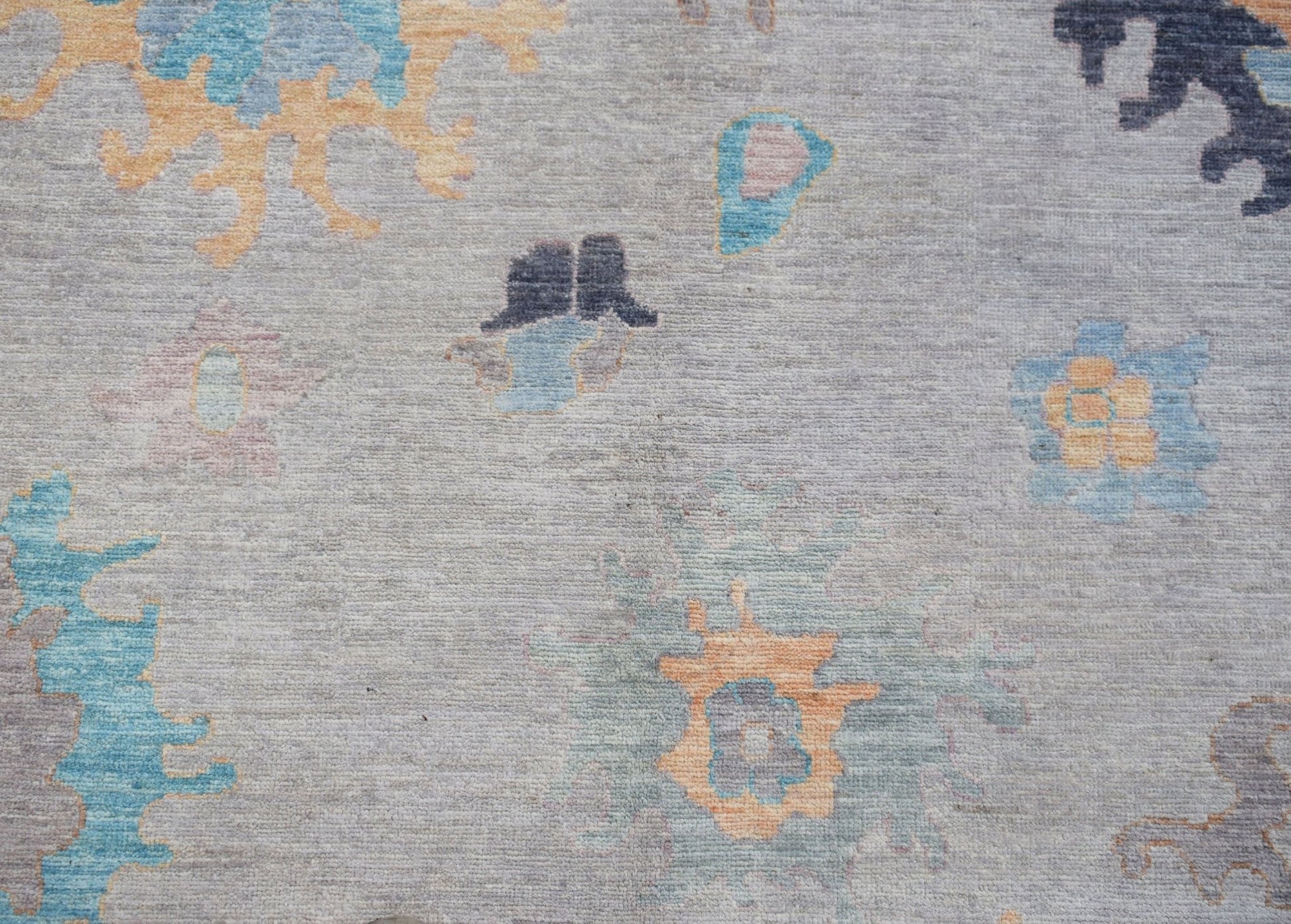 A handwoven transitional Oushak rug featuring a floral pattern in blue and orange on a grey field.
